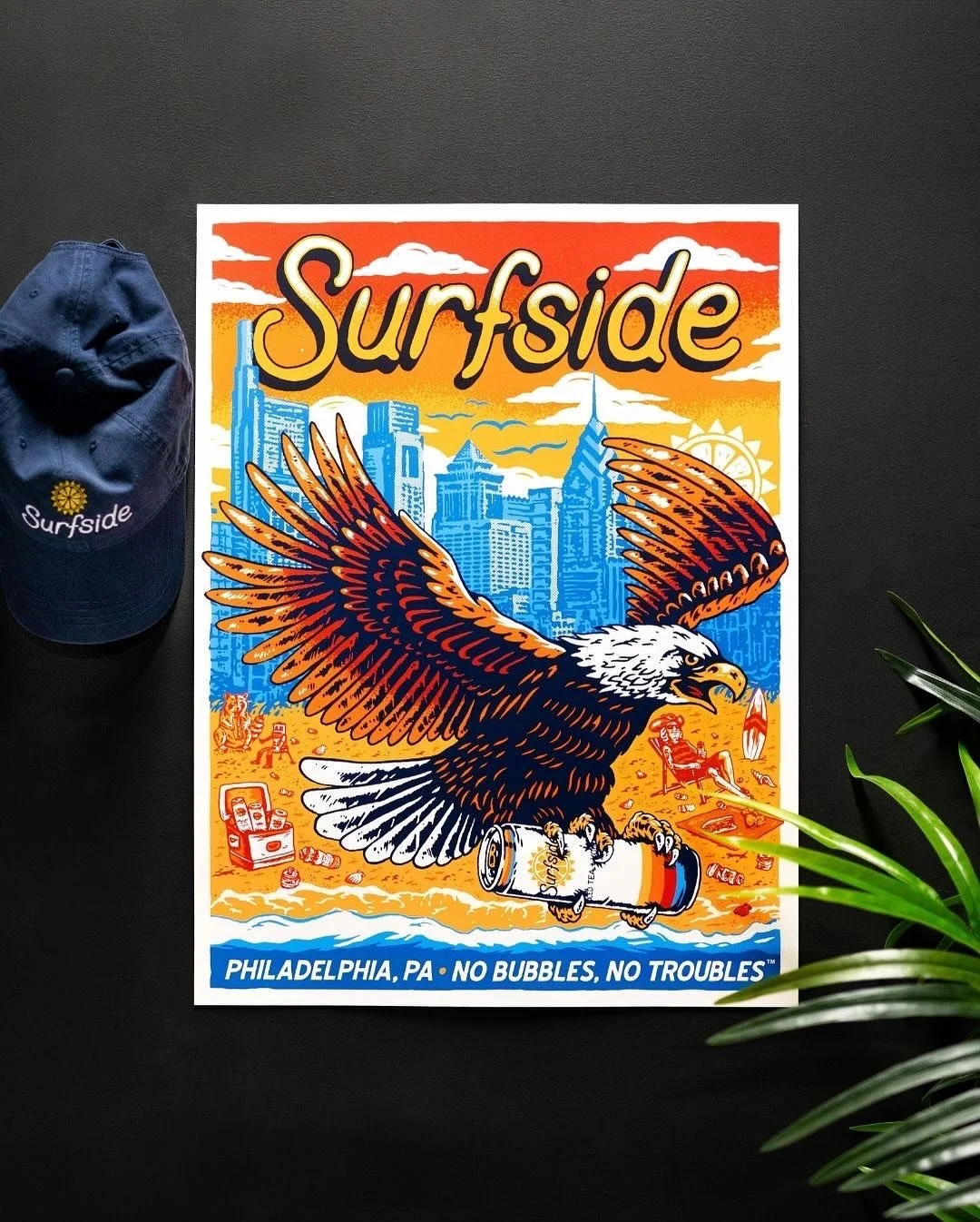 A colorful surfside poster with a flying eagle holding a soda can, set against a cityscape background, with a blue cap on the left and a green plant on the bottom right.