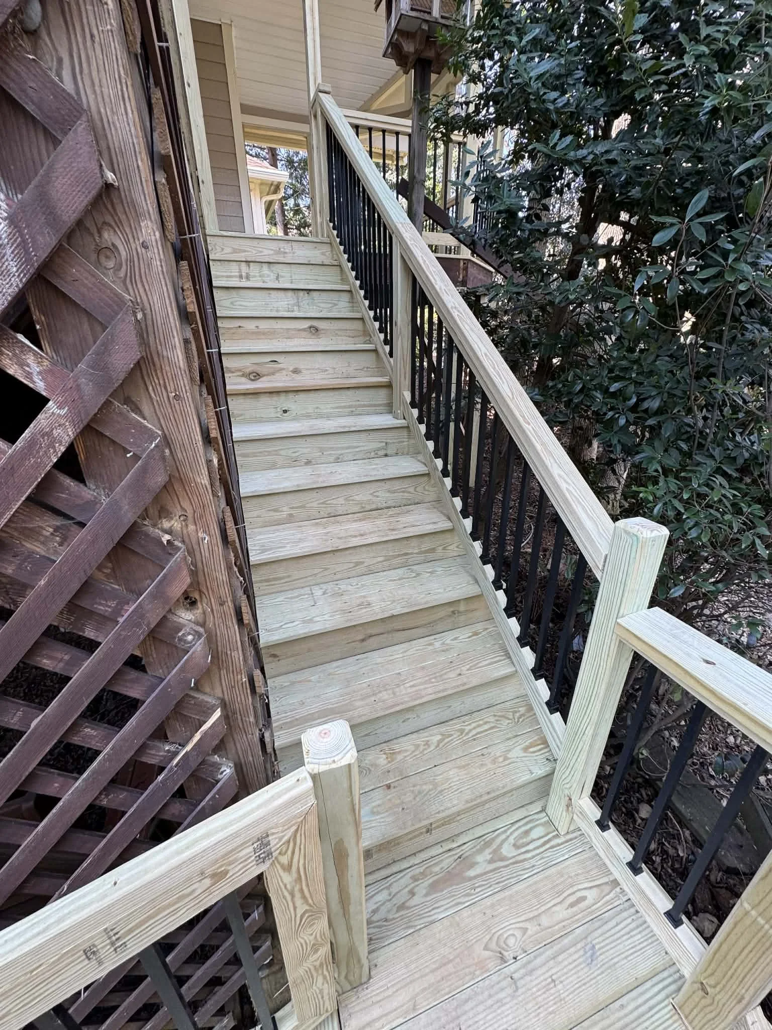 Newly constructed wooden outdoor staircase with black metal railings next to a house and surrounded by trees.