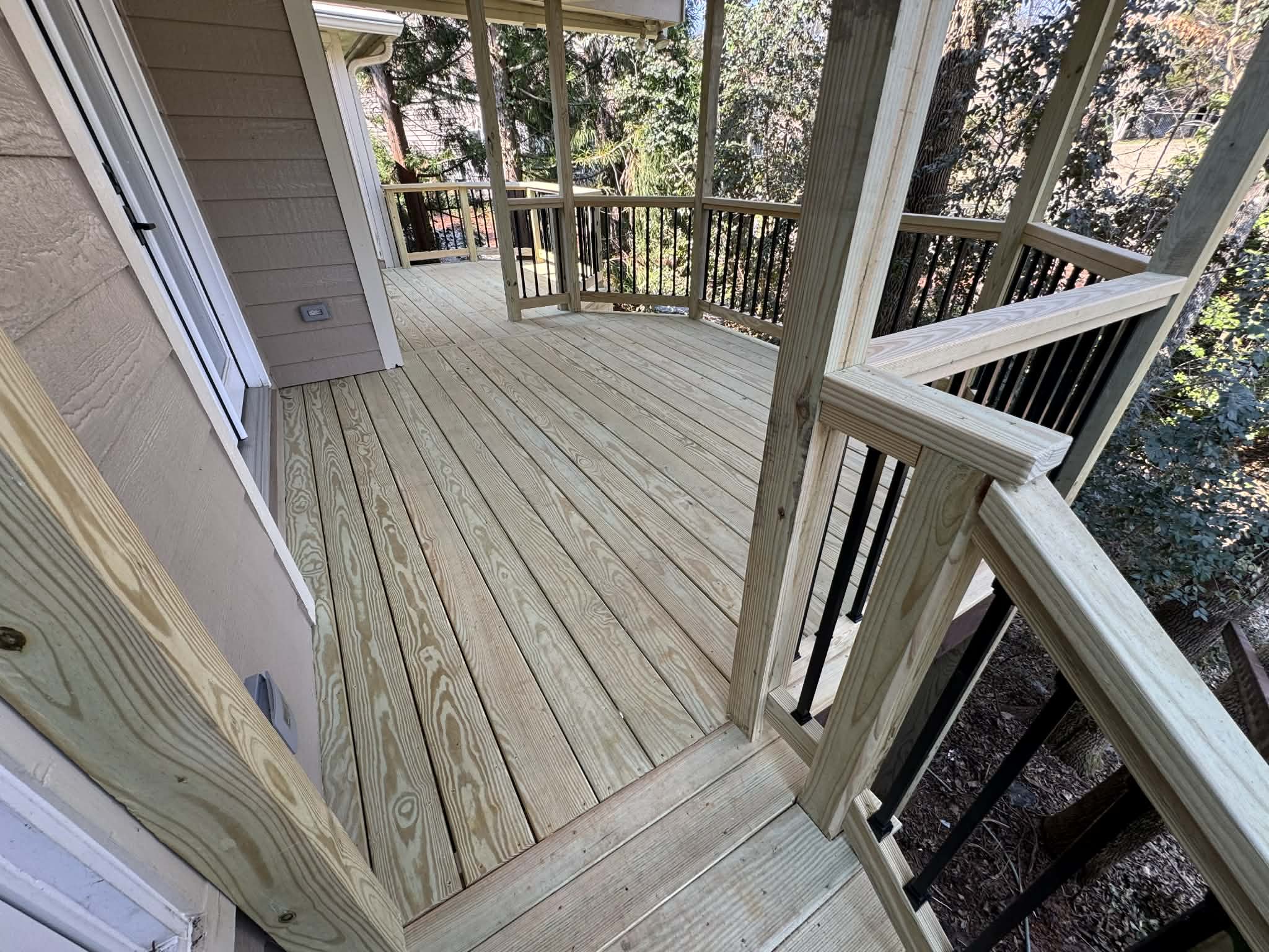 Freshly built wooden deck with railing attached to house, surrounded by trees.