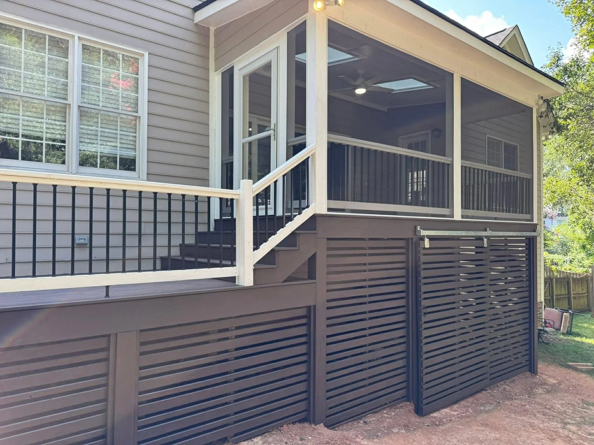 Exterior view of a house with a screened-in porch and black slatted privacy fencing below, stairs leading up to the porch, and a glass-paneled door.