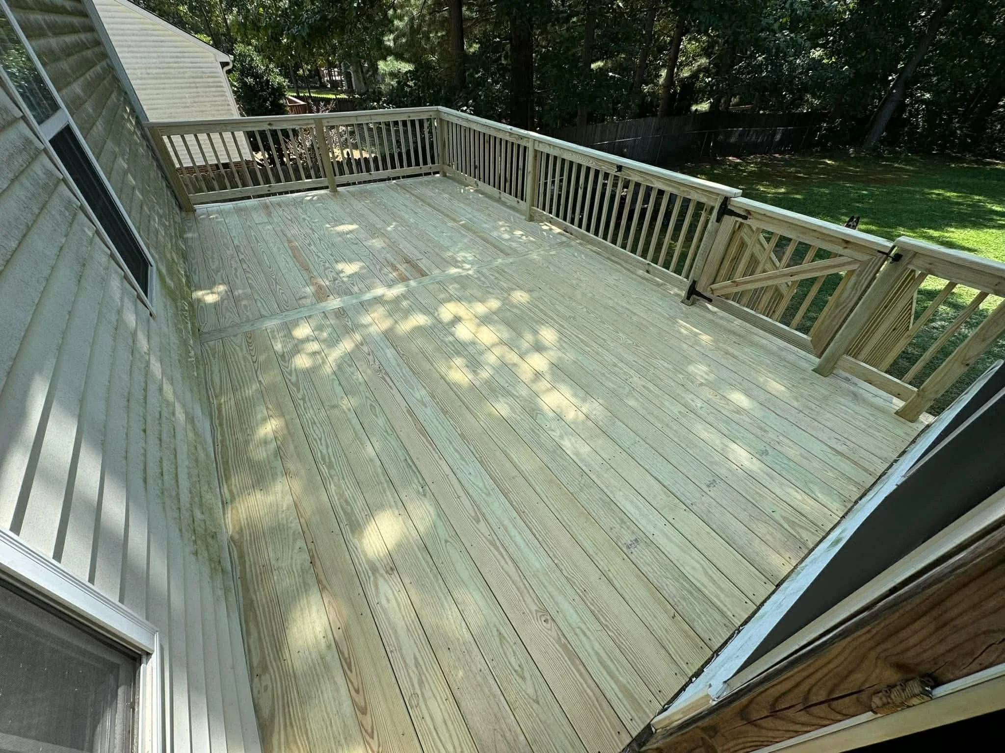 Freshly built wooden deck with railing, partial view of house, trees, and backyard.