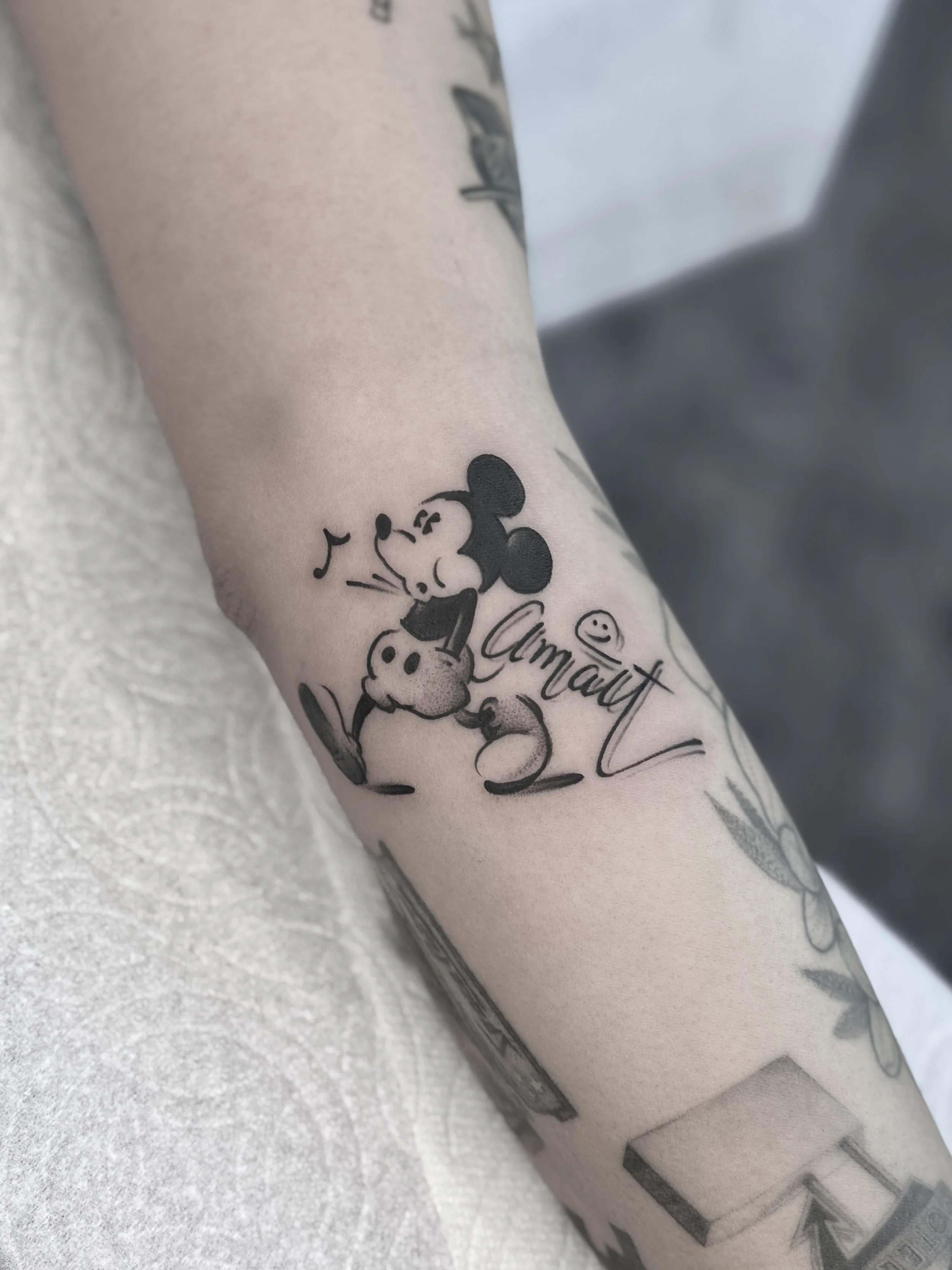 Custom black and grey Mickey Mouse tattoo paired with the artist’s “AMART” signature. Client traveled internationally for this piece.