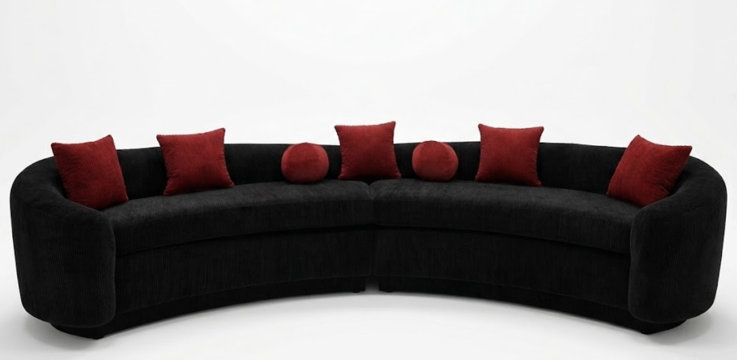 A long black curved sofa with six red pillows, three square and three round, set against a white background.