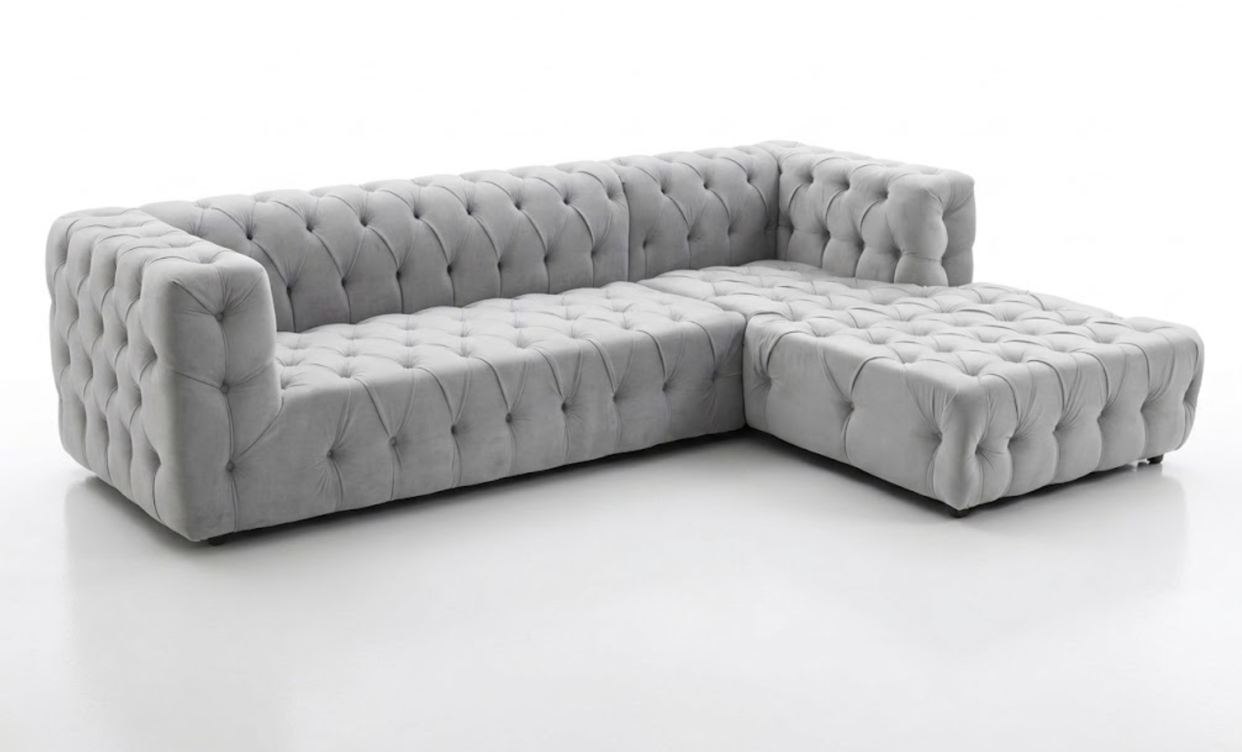 Light gray tufted fabric sectional sofa with a chaise lounge, set against a white background.
