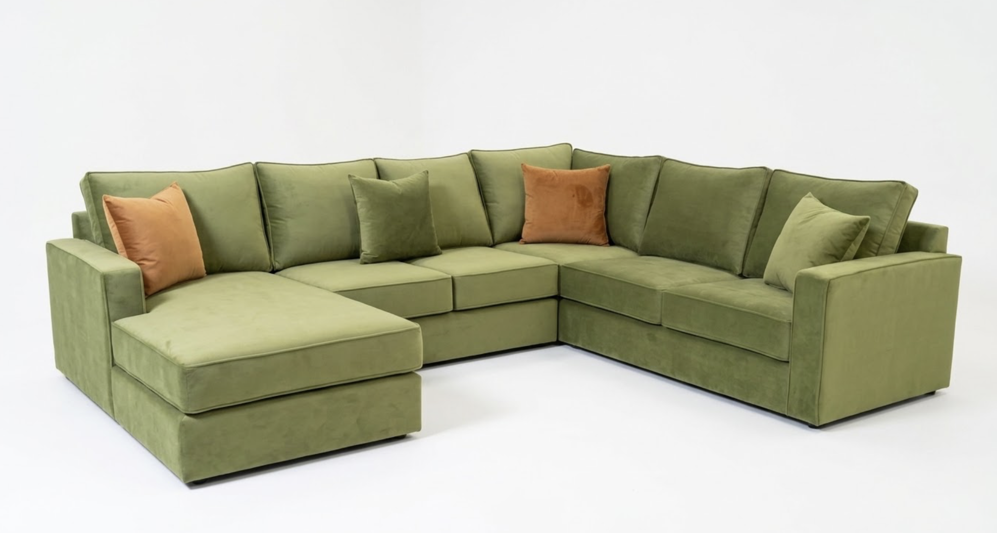 A large green sectional sofa with multiple cushions, including two orange and three green pillows, set against a plain white background.
