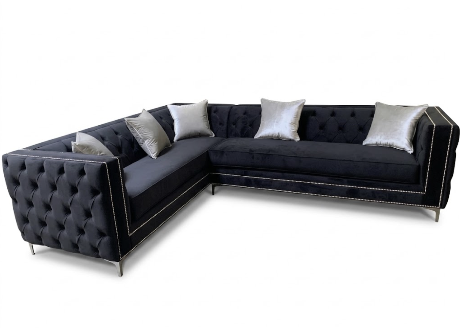 Black velvet L-shaped sectional sofa with tufted design and silver nailhead trim, decorated with silver pillows.