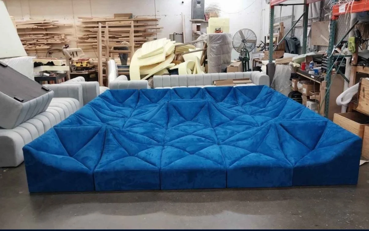 A large, modular, bright blue upholstered sofa with a quilted pattern in a workshop or warehouse setting.