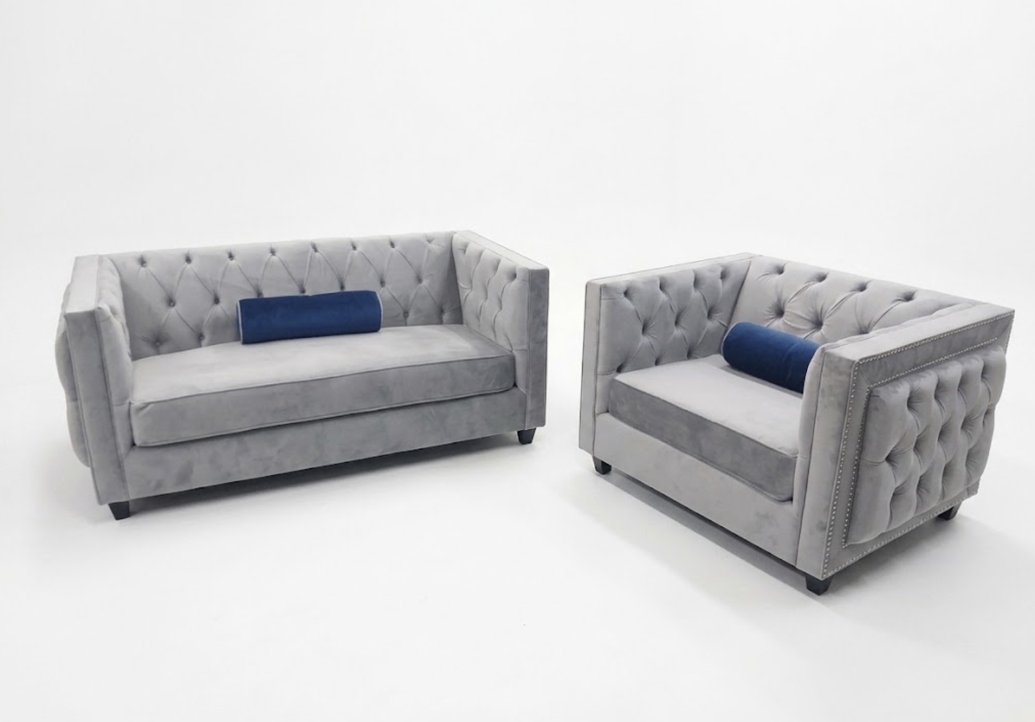 Two gray tufted sofas with dark wooden legs and blue cylindrical pillows on a white background.