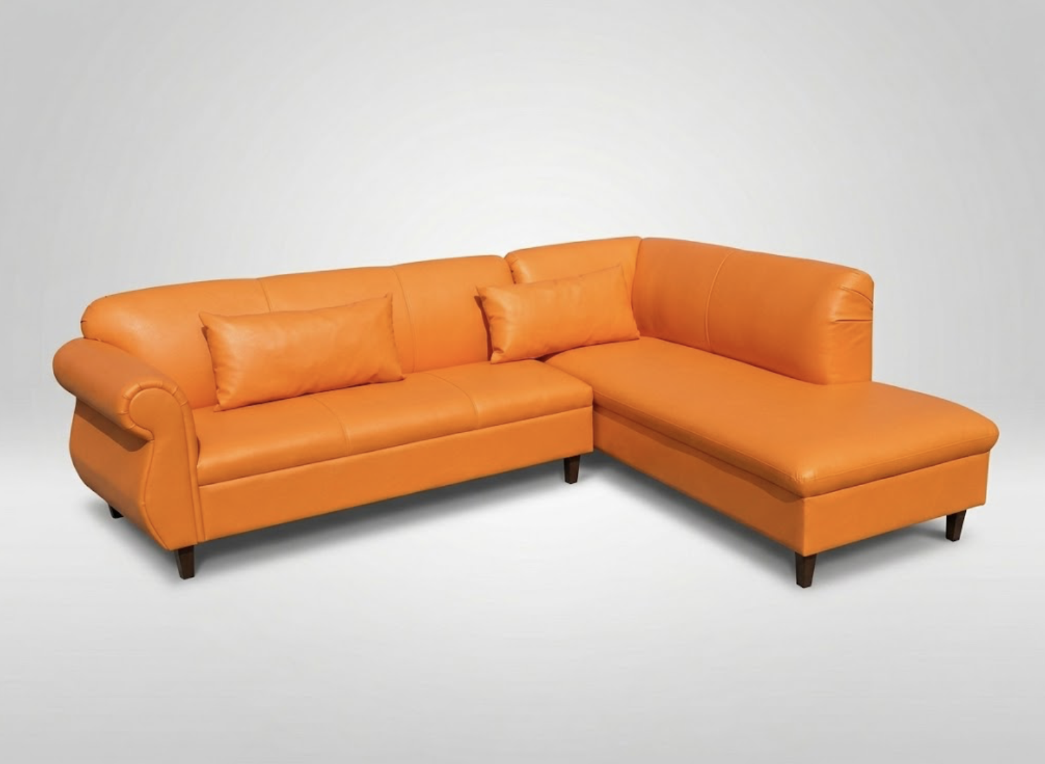 Orange leather L-shaped sofa with two matching pillows, set against a plain white background.