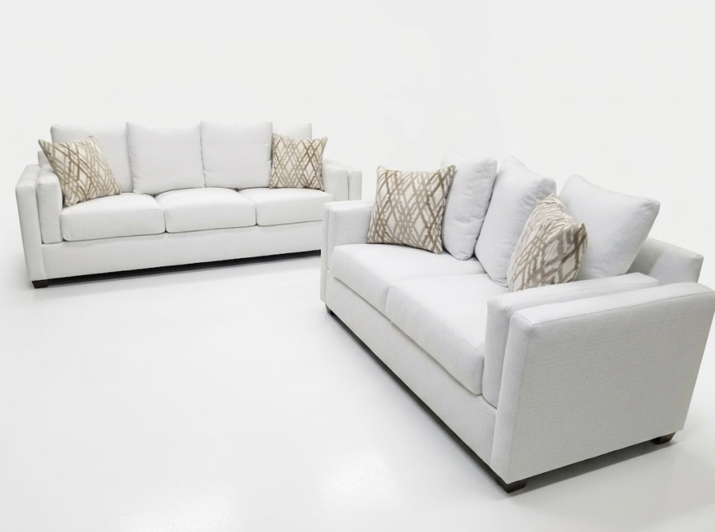 Two white sofas with beige patterned throw pillows in a minimal white room.