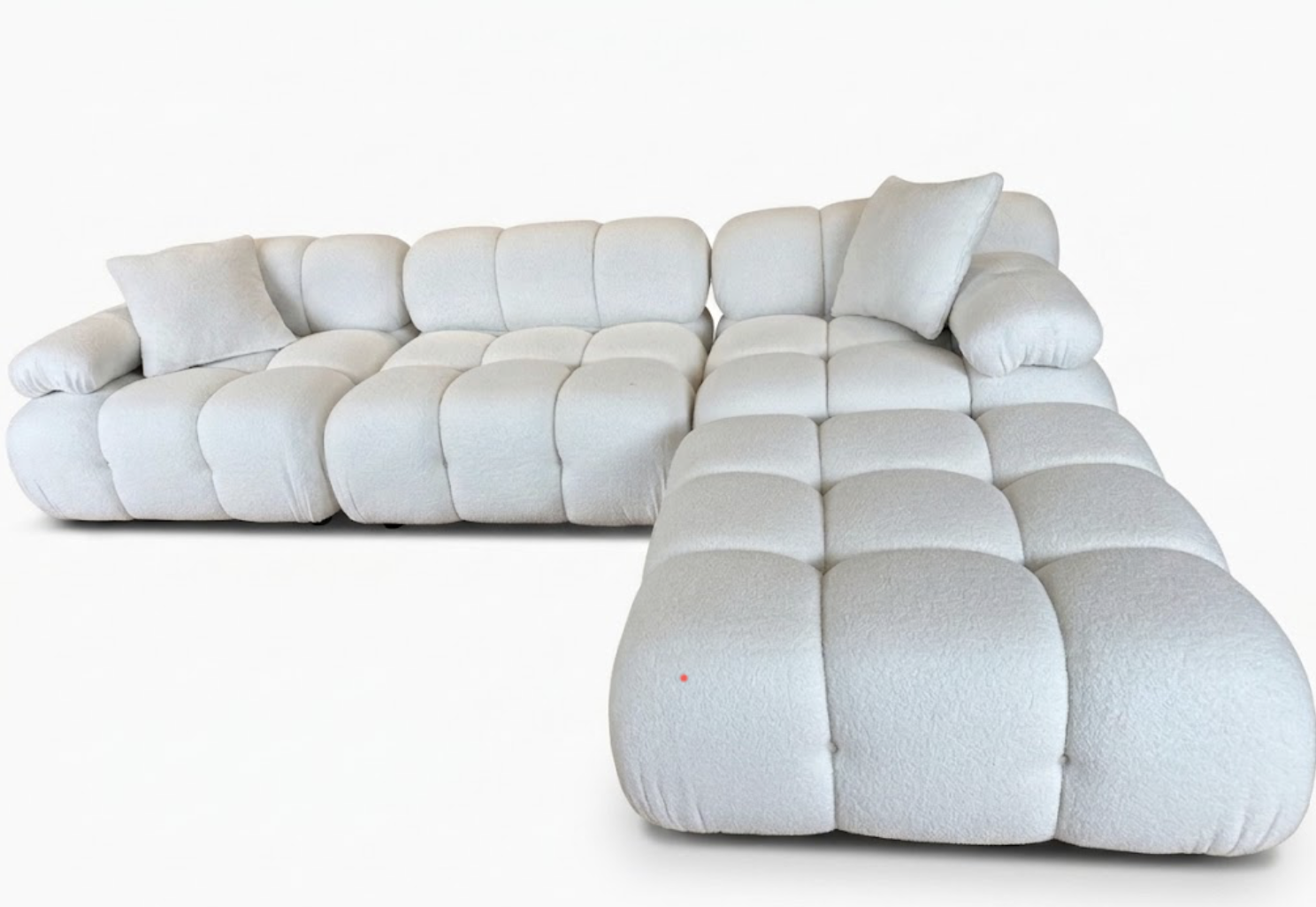 A white sectional sofa with matching pillows, featuring a modern, plush, tufted design against a plain white background.