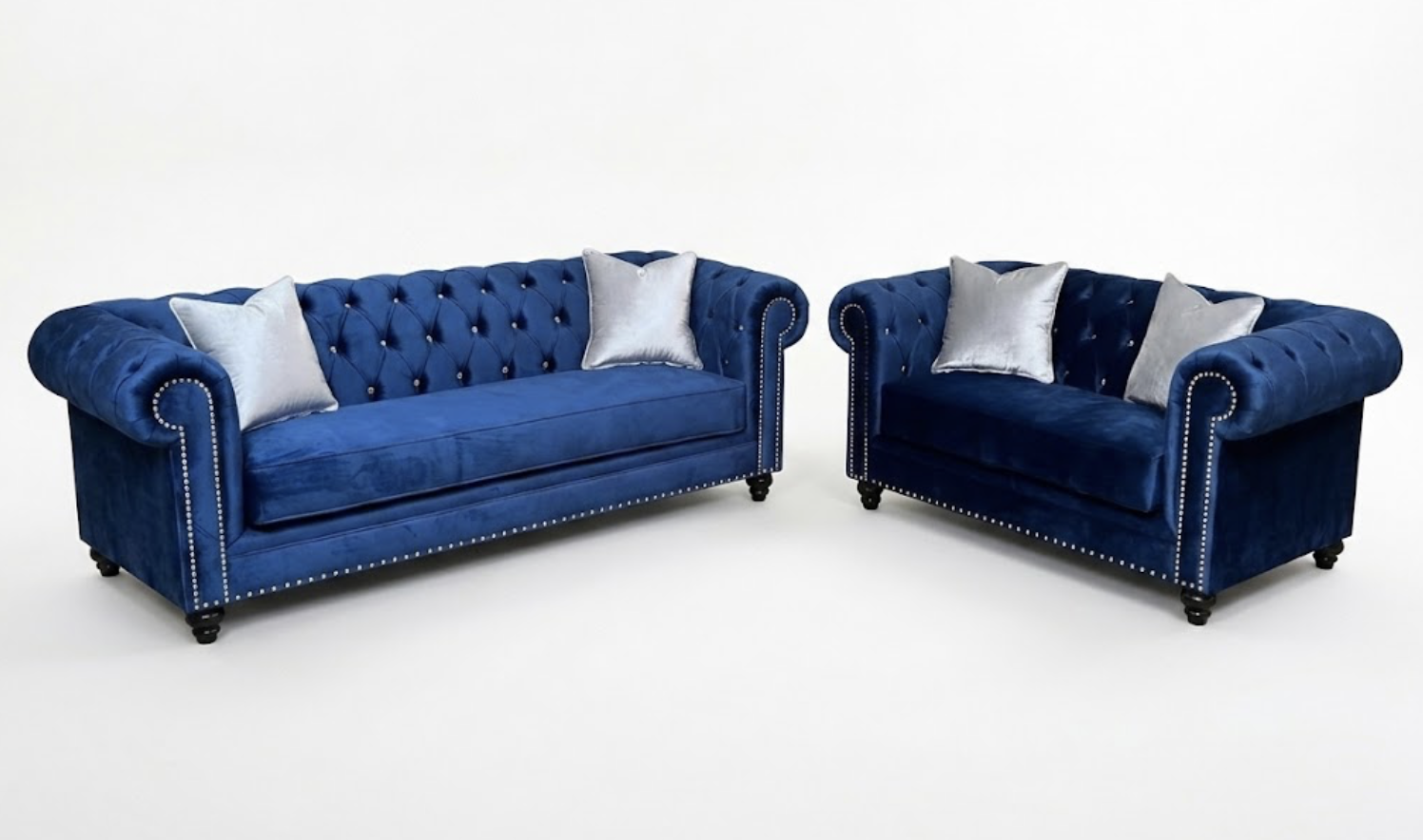Two matching blue velvet upholstered sofas with silver throw pillows against a plain white background.