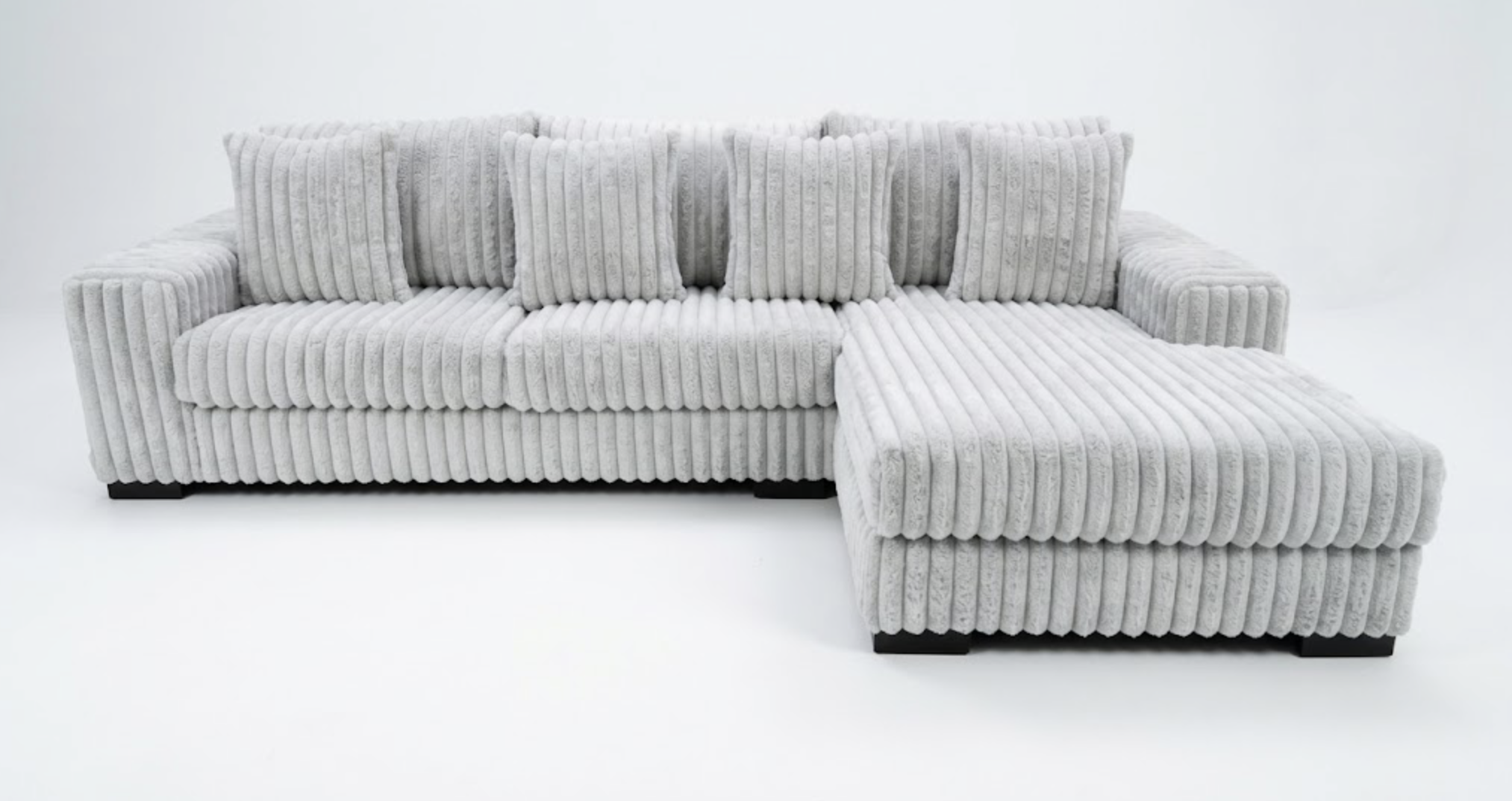 A white, plush, corduroy sectional sofa with matching ottoman in a minimalist setting.