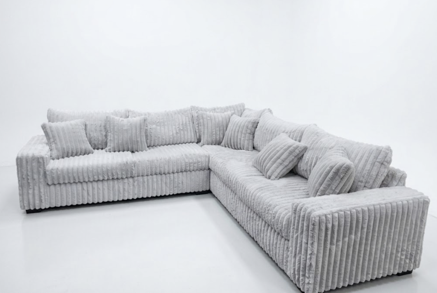 A large, light gray, textured sectional sofa with matching pillows in a plain, white room.