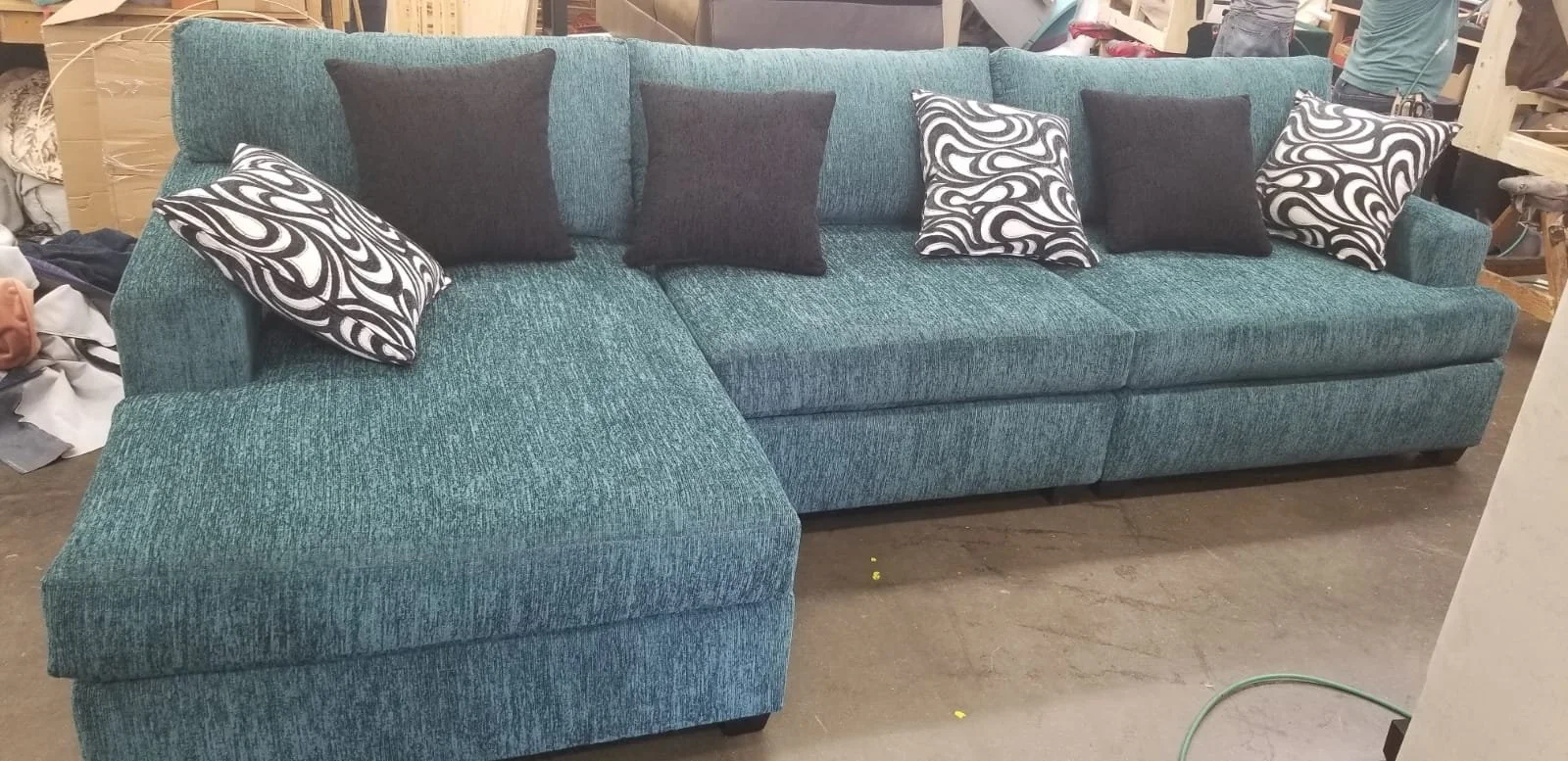 A teal-colored sectional sofa with black and patterned pillows in a furniture store.