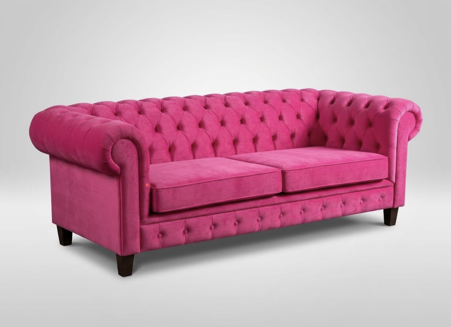 Pink tufted velvet sofa with rolled arms and wooden legs on a plain gray background.