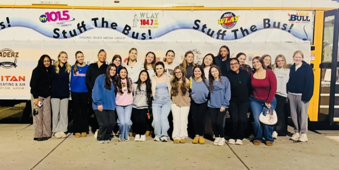 Group of young women and girls posing in front of a bus with 'Stuff The Bus!' advertising on it.