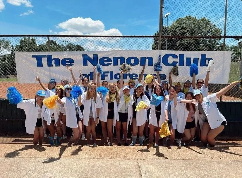 A group of young girls dressed as cheerleaders, some in lab coats, celebrating on a tennis court with a banner that reads 'The Nemon Club Flareletes'.