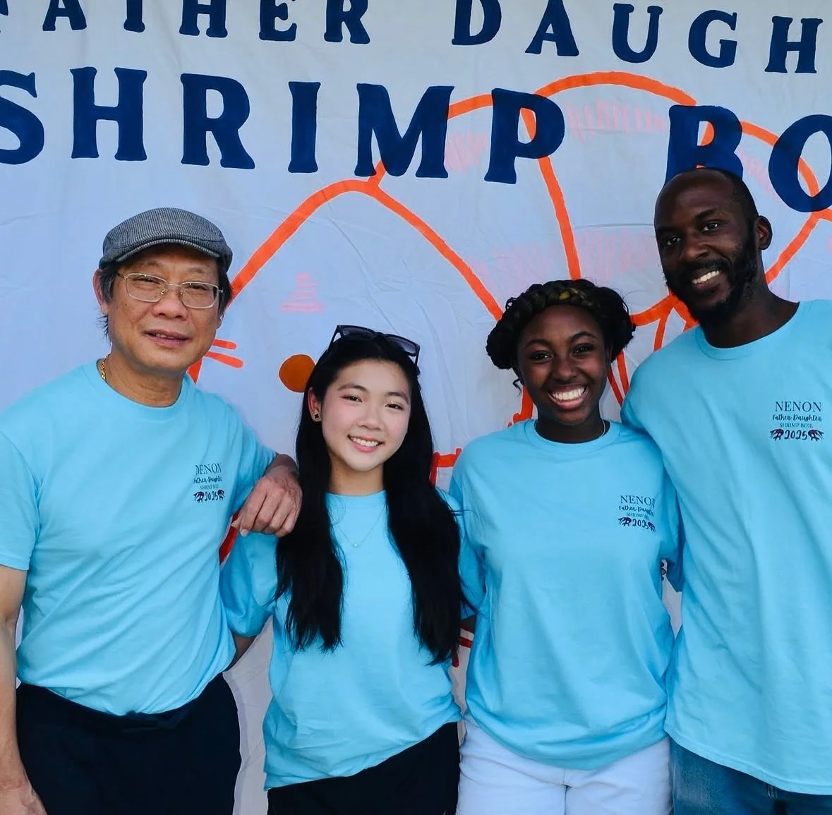 Four people standing in front of a banner that reads 'Father Daughter Shrimp Bo'. They are wearing matching light blue shirts.