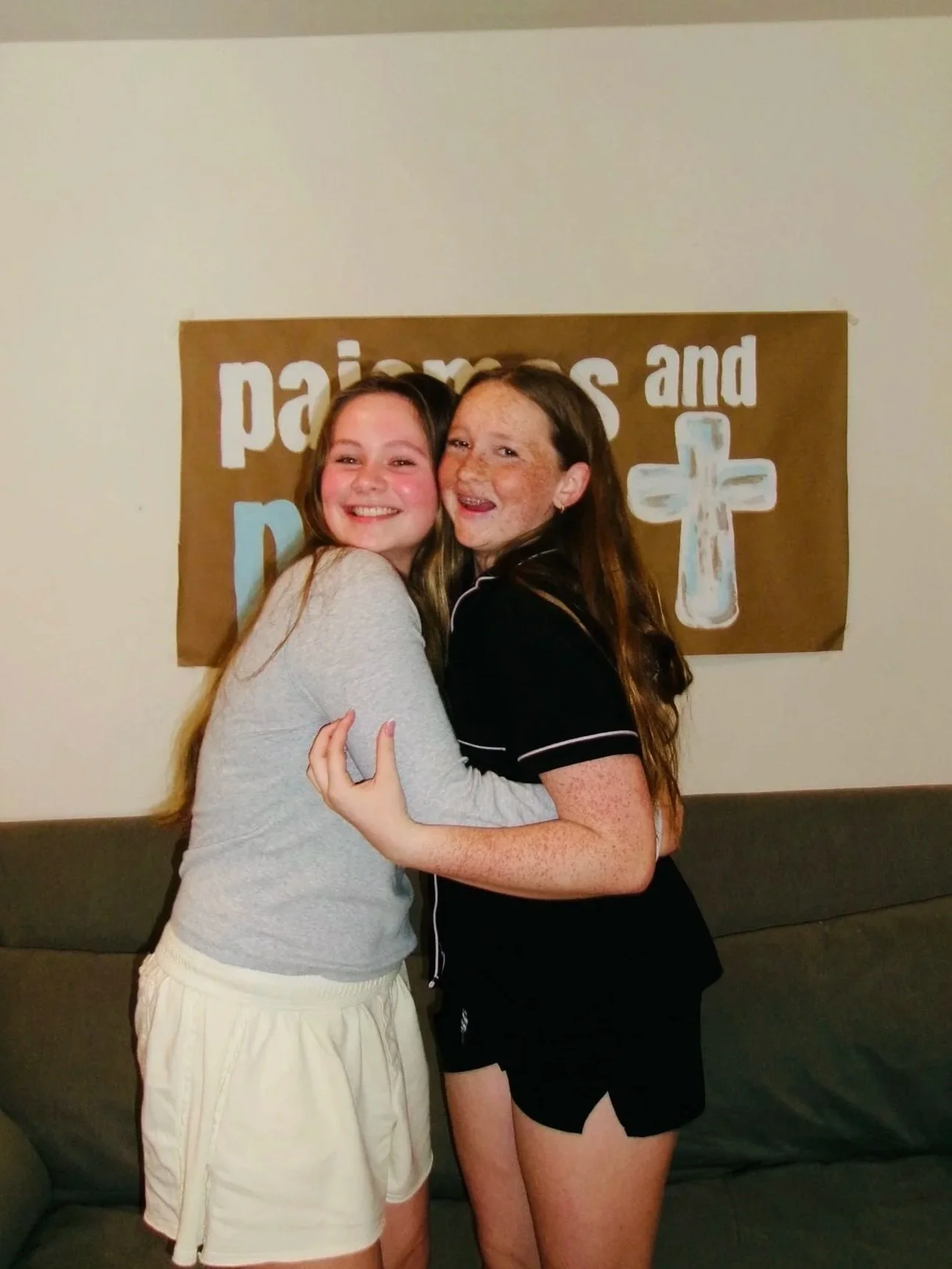 Two girls hugging and smiling in front of a church-themed banner.