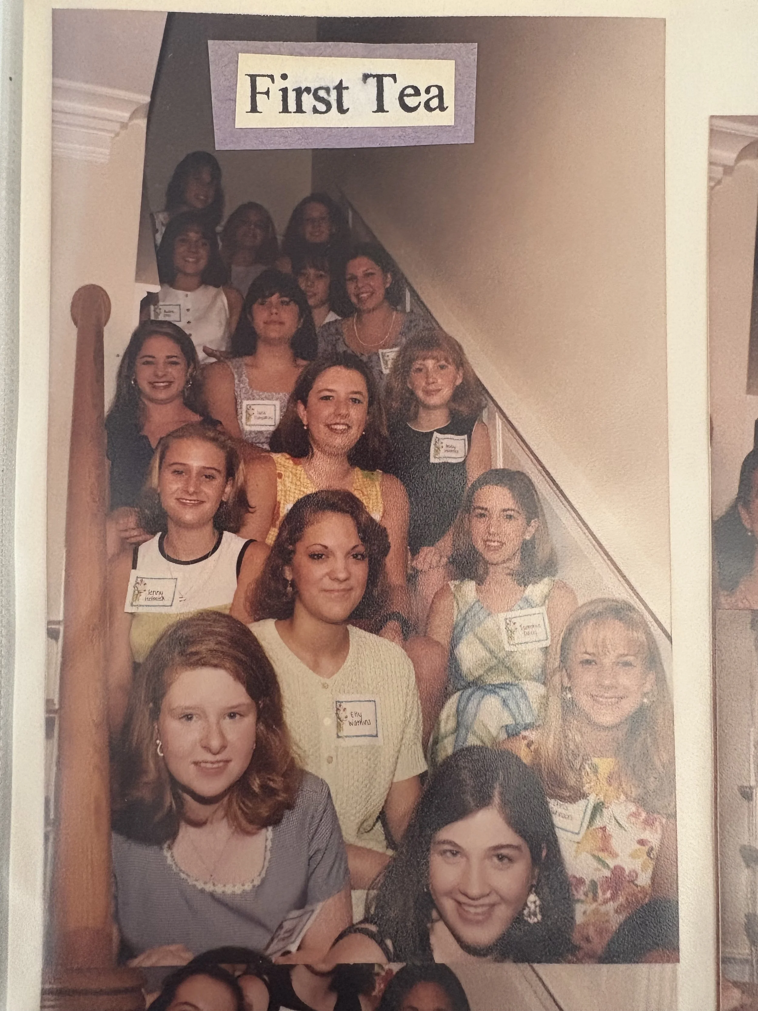 Group of women and girls on a staircase, with a sign reading "First Tea" at the top.