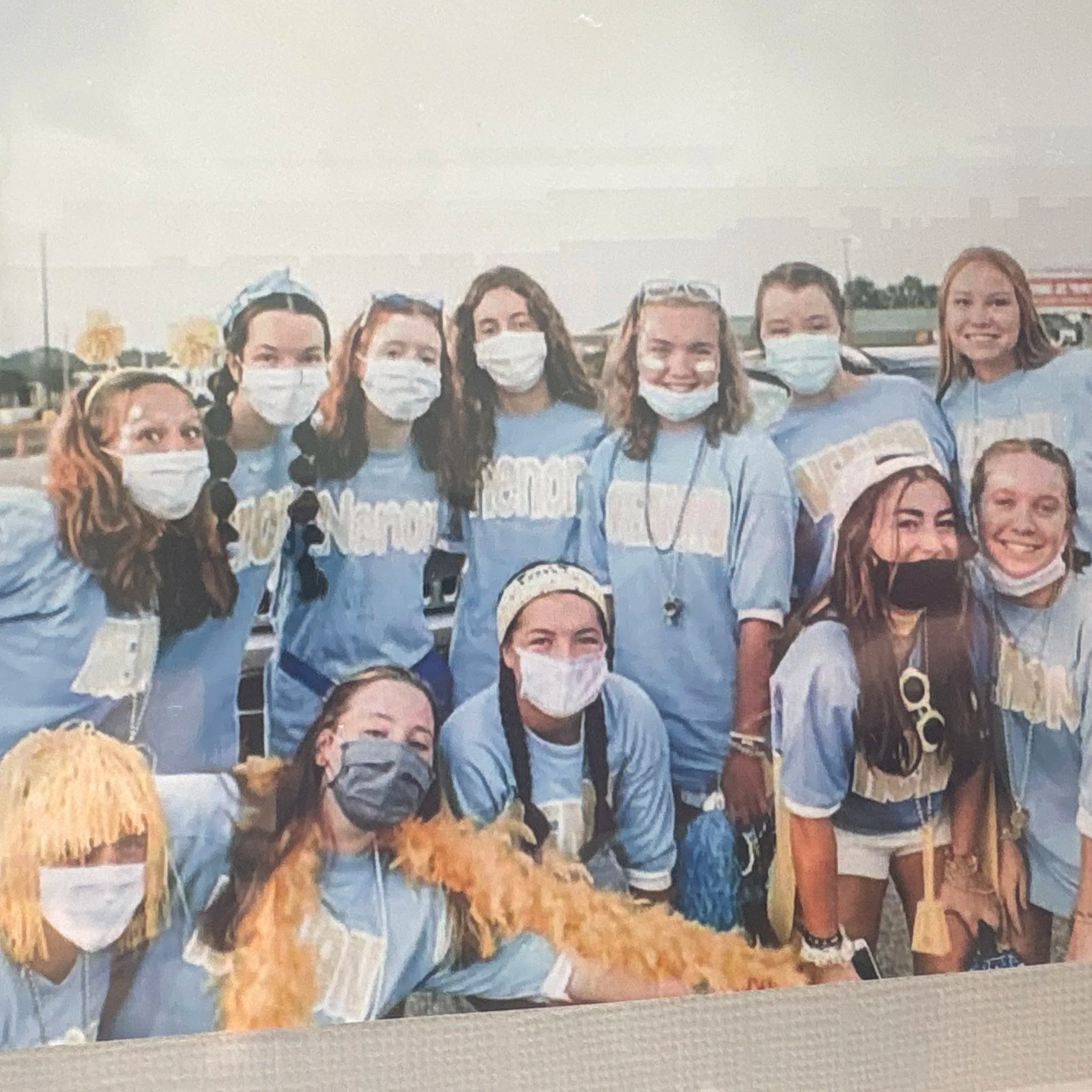 A group of girls and women wearing matching light blue T-shirts and face masks, gathered outdoors during daytime.
