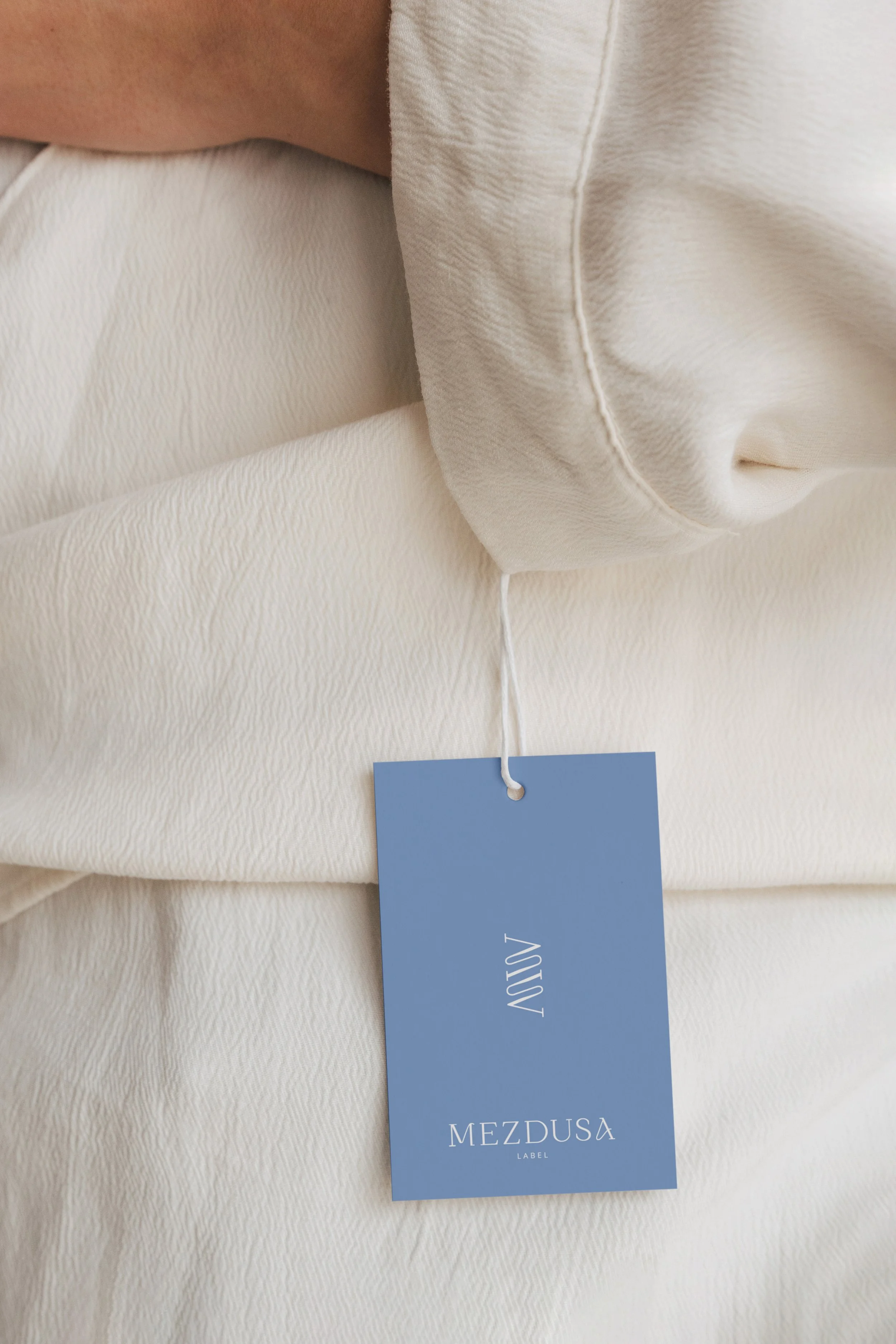 Close-up of a light-colored blazer with a blue tag that reads 'ADOVA' and 'MEZDUSA LABEL'.