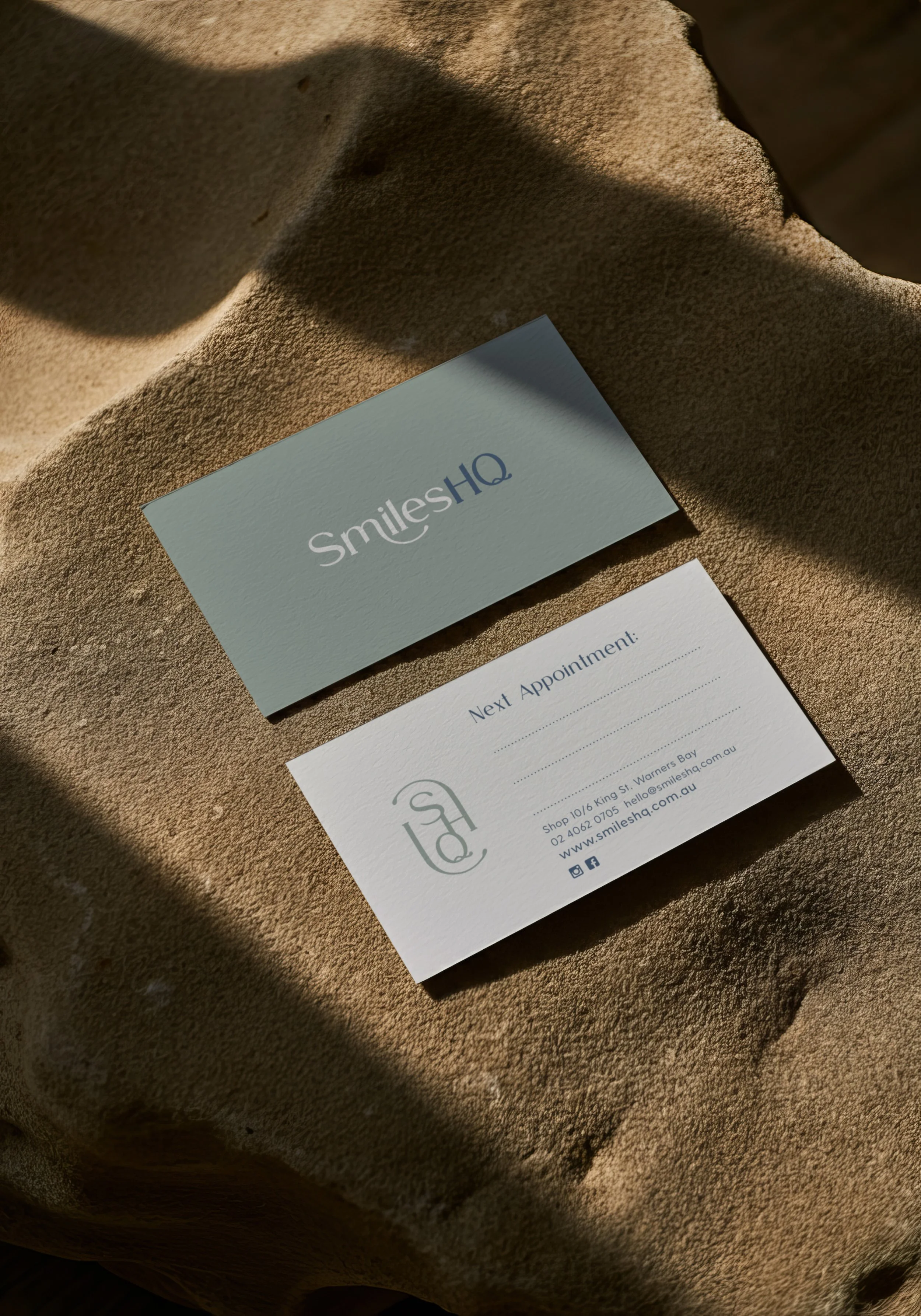 A business card and appointment card for SmileSHQ on a textured brown surface with shadows.