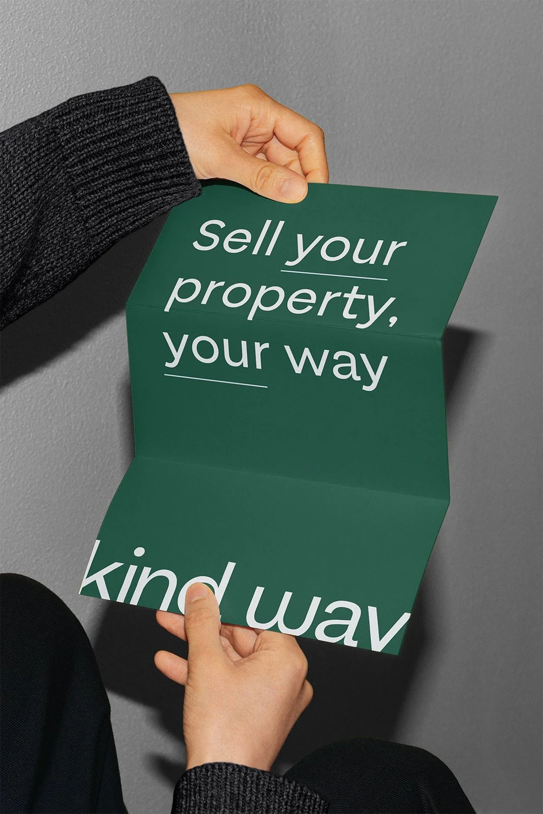 Hands holding a green folded sign with the message 'sell your property, your way' printed on it.
