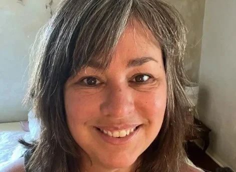 Close-up of a woman with shoulder-length gray hair smiling indoors.