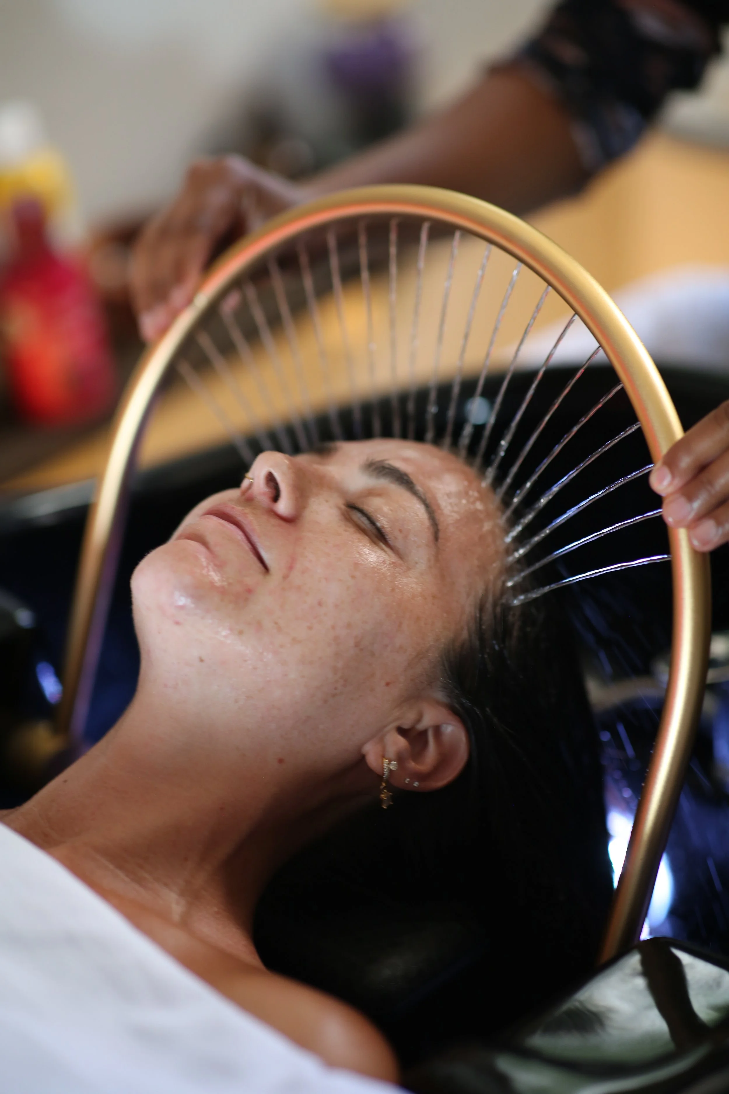 A woman giving a korean head spa treatm to a person lying face up with the water cascading over her head