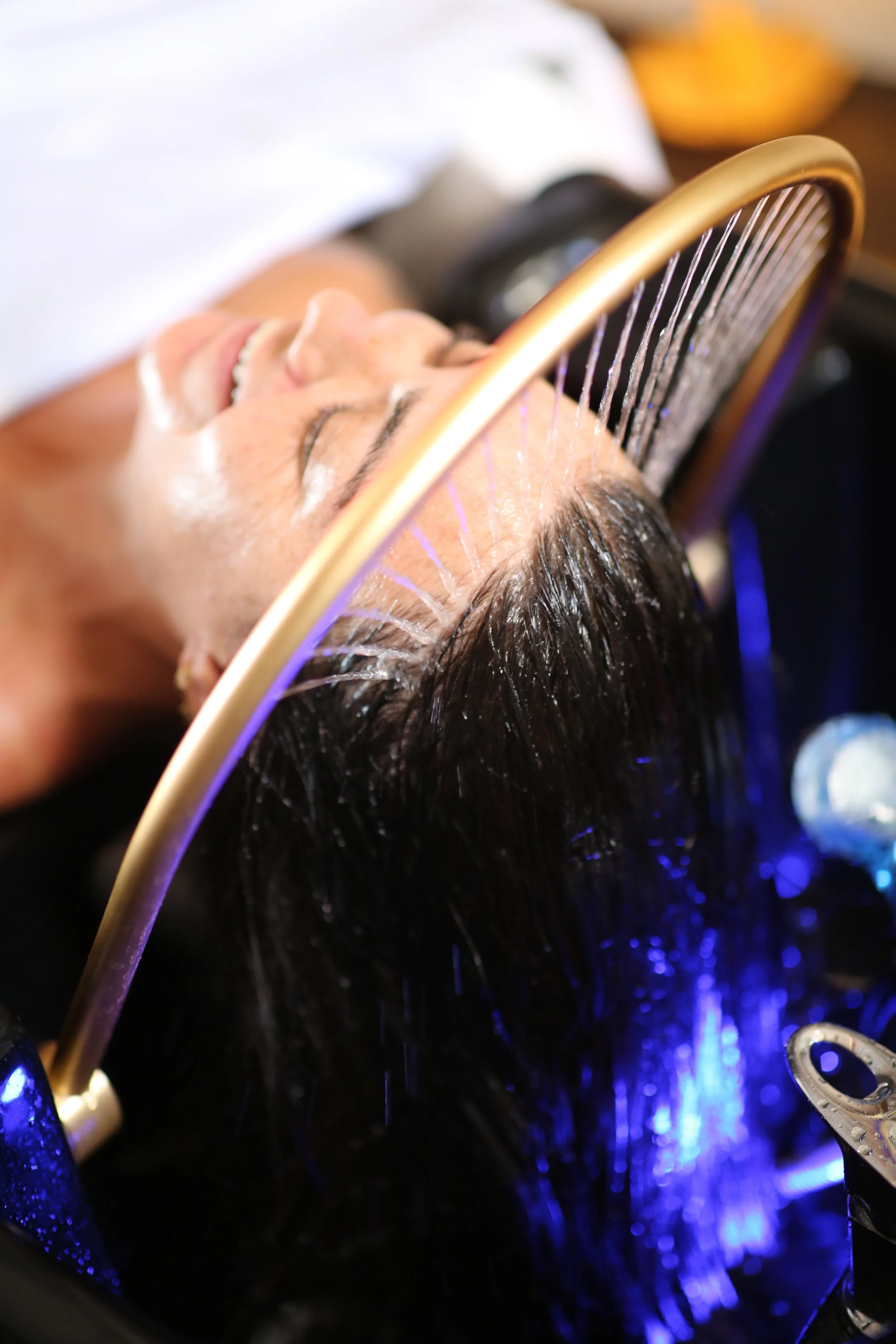 A person lying down, holding a cotton pad or towel to their face, with herbal oil is gently and continuously streamed across the forehead ("third eye")