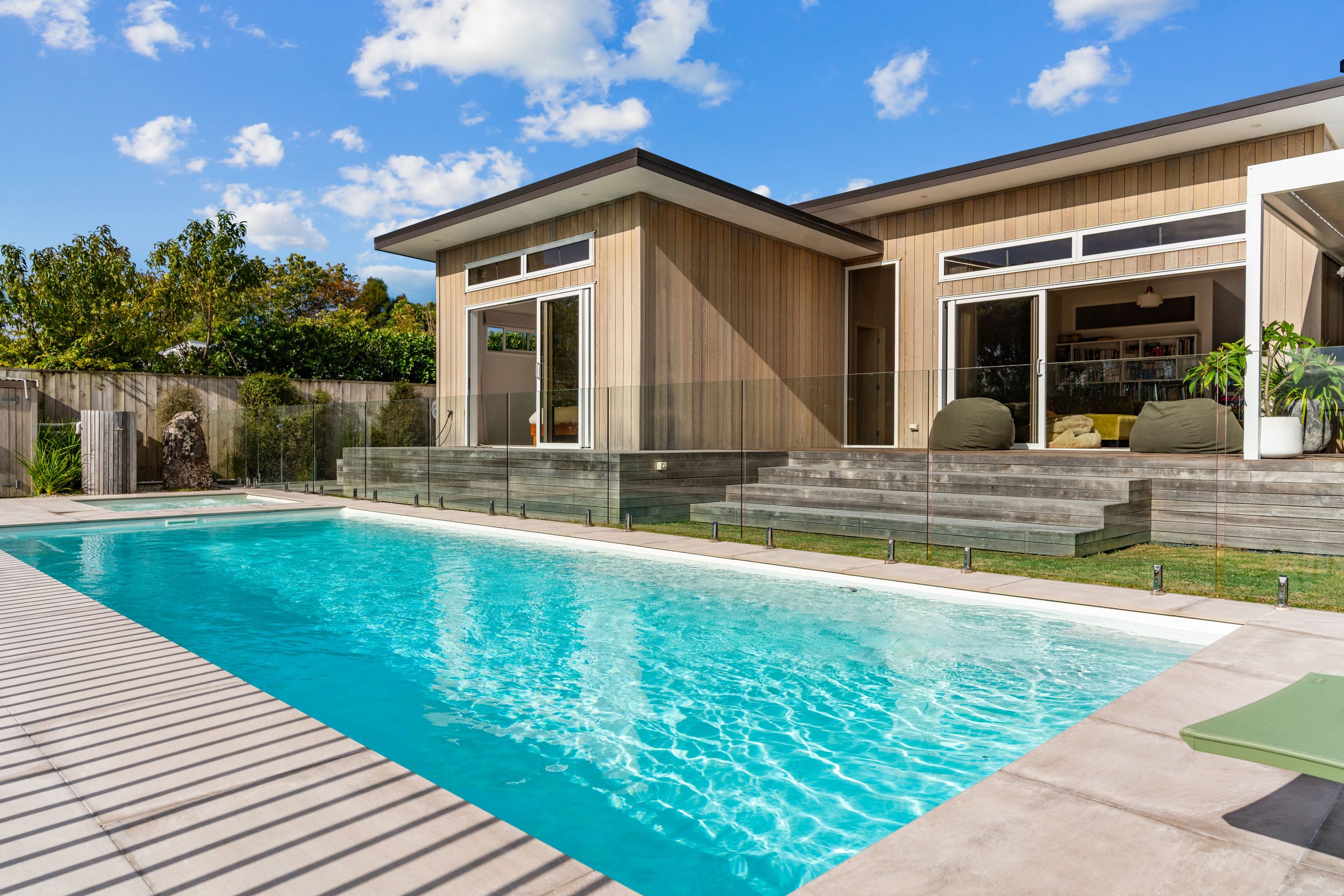 Modern house with large swimming pool in backyard under blue sky with clouds