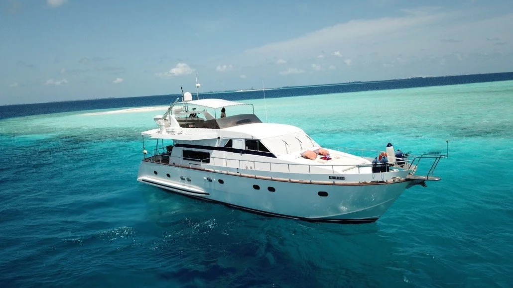 A white yacht floating on clear blue ocean water near a coral reef
