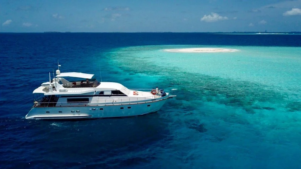 White yacht sailing in clear blue ocean near a floating sandbar or coral reef