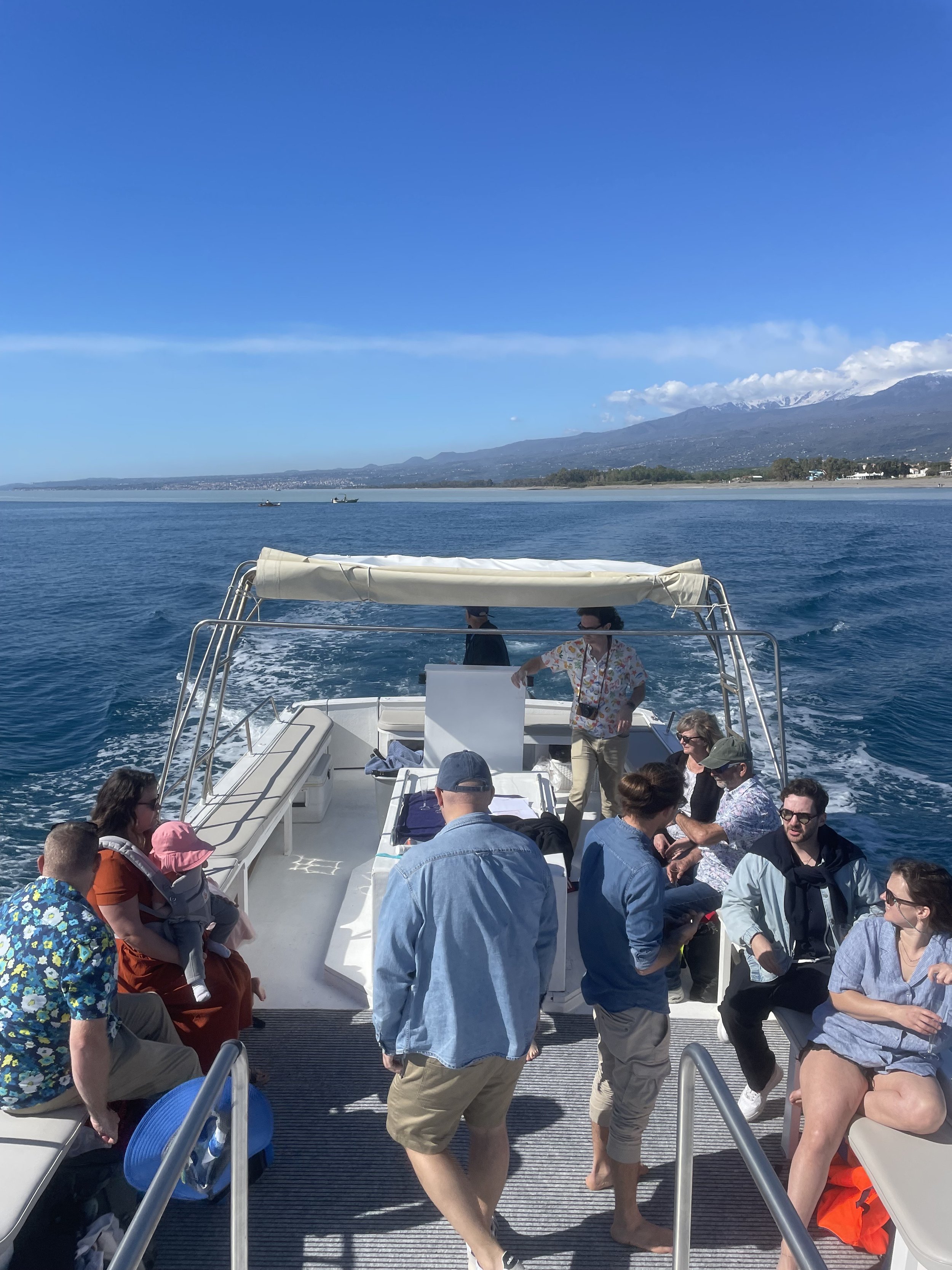 Group of people enjoying a boat ride on a sunny day with mountains and coastline in the background.