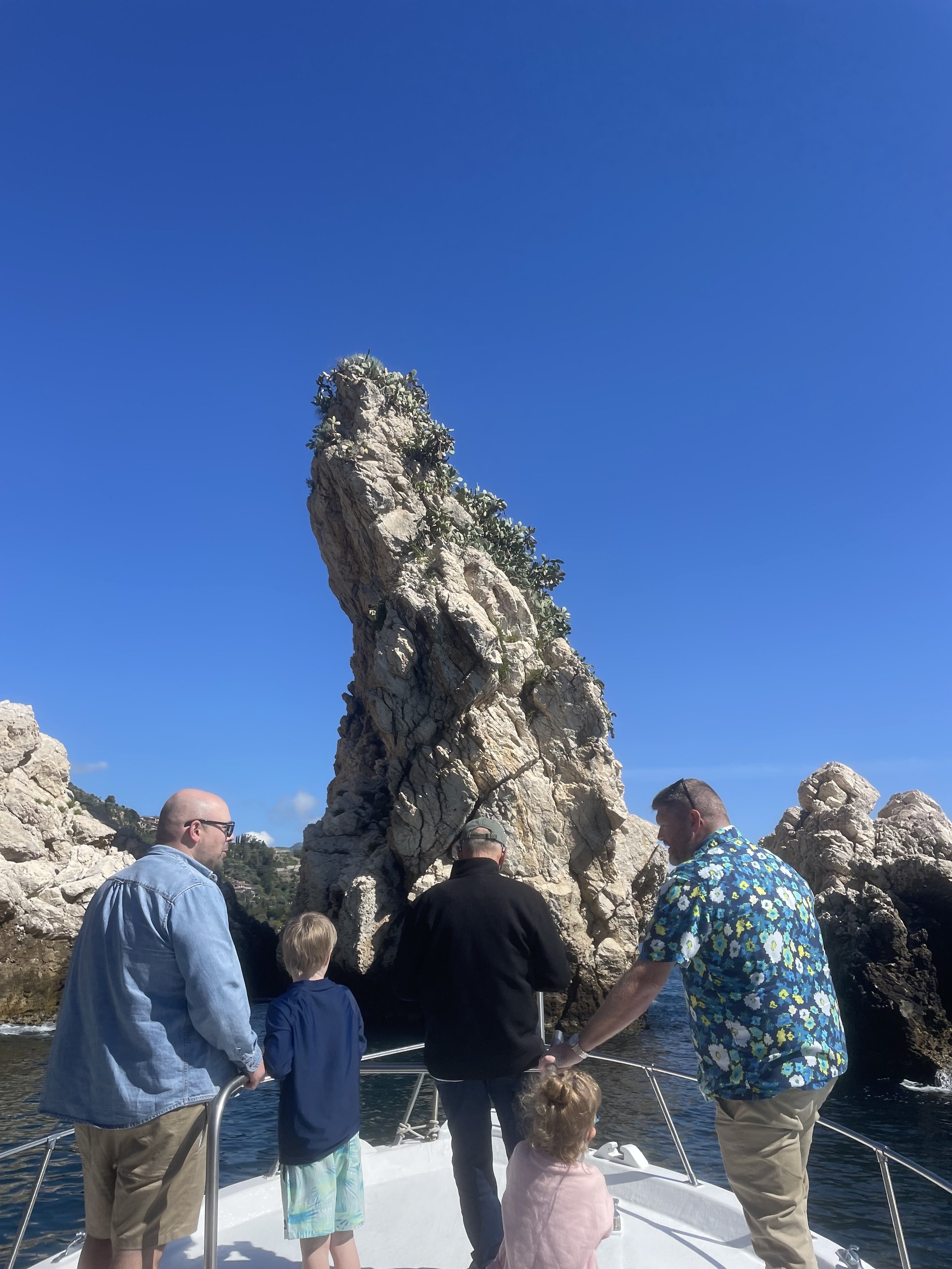 A group of people on a boat approaching large rock formations in the sea under a clear blue sky.