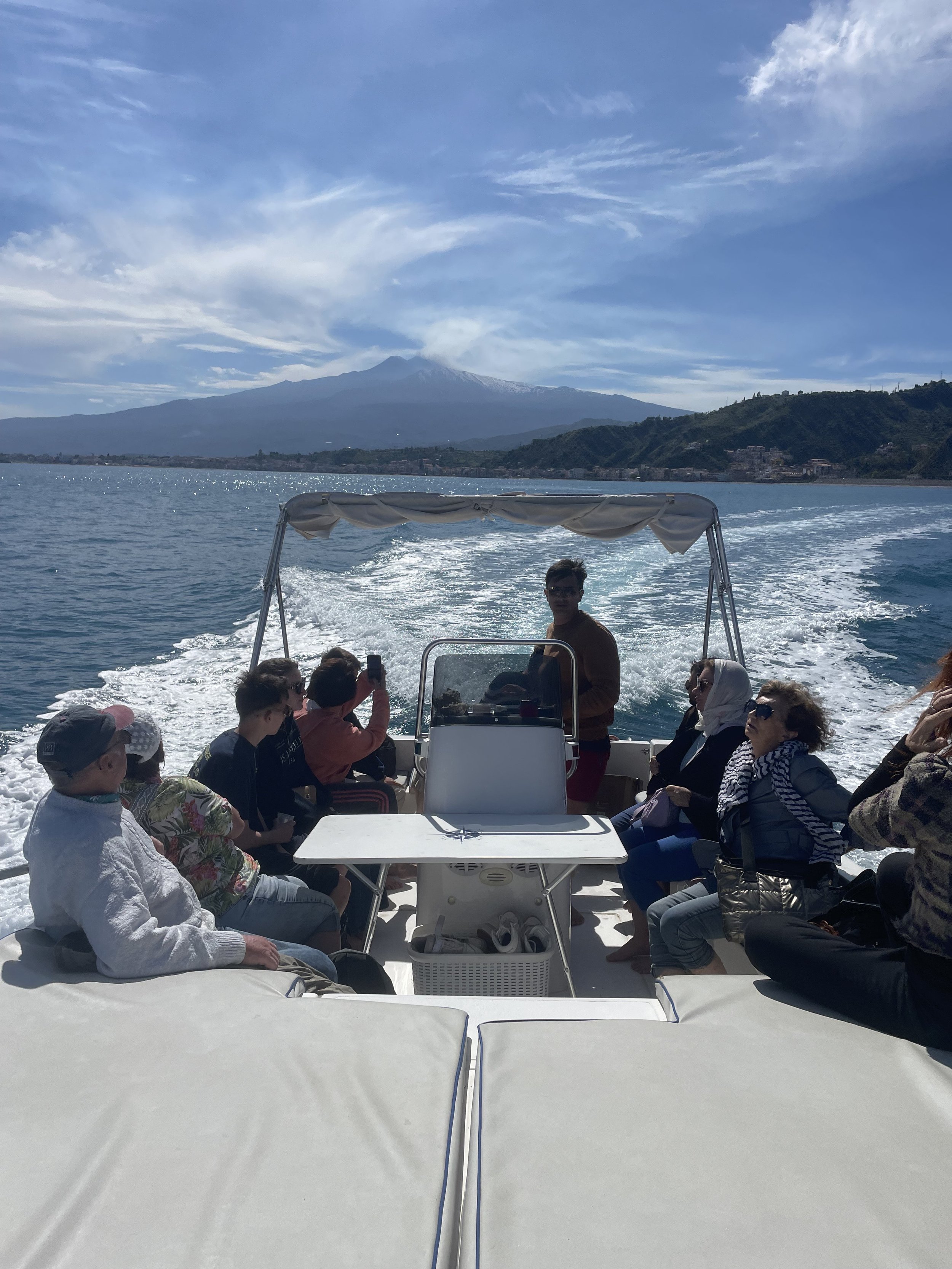 People sitting on a boat with a scenic view of a distant mountain, ocean, and cloudy sky.