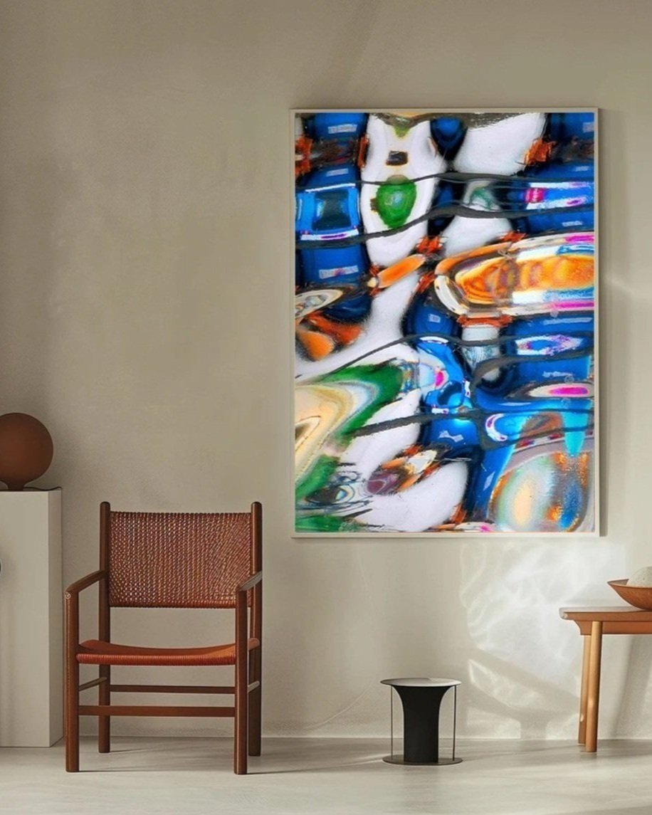A modern room with a colorful abstract painting on the wall, a wooden chair with woven seat and backrest, a small black and white side table, and a wooden console with a bowl, all illuminated by natural light.