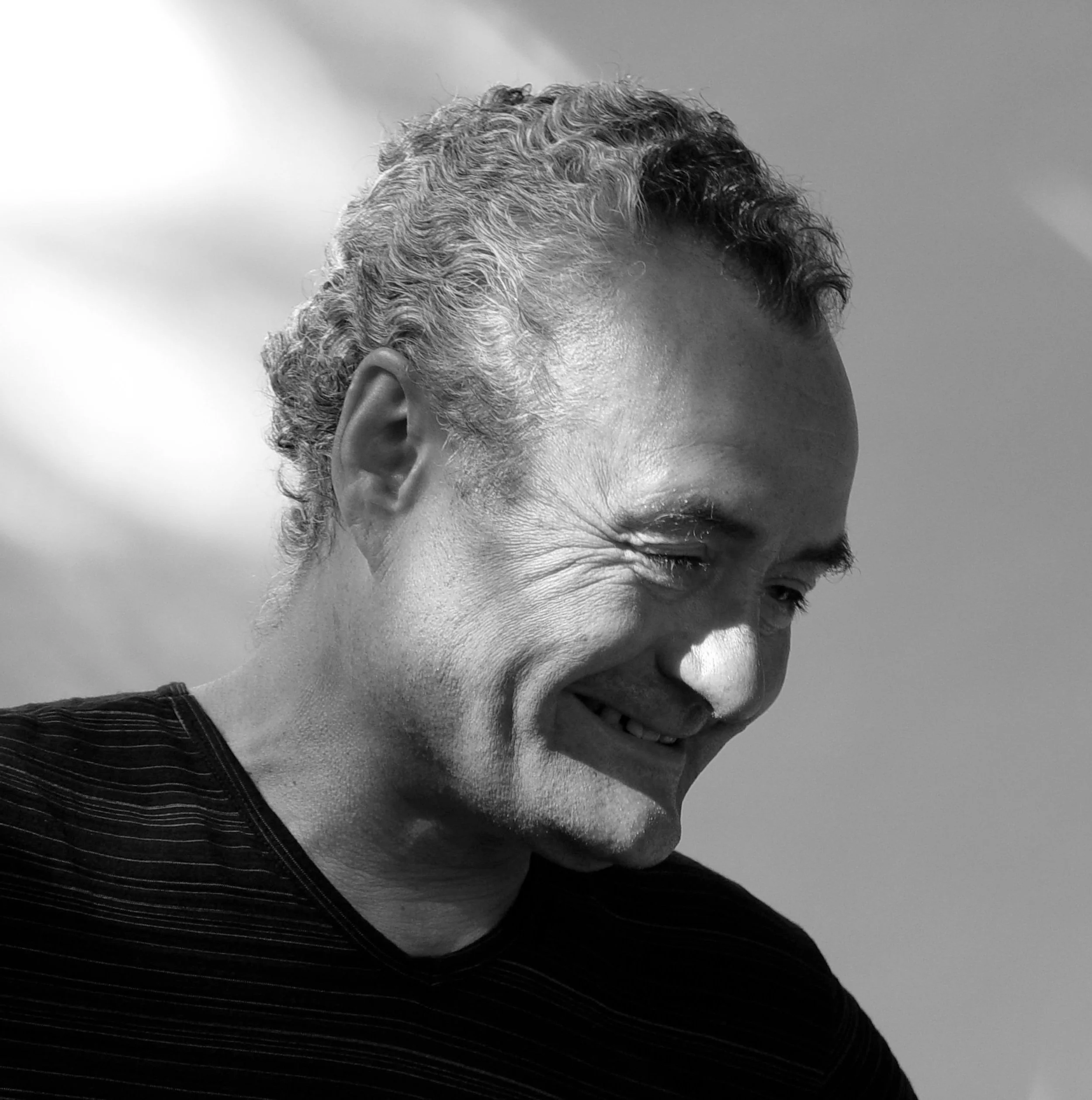 Close-up shot of a person with curly hair, smiling, wearing a pinstripe suit, in black and white.