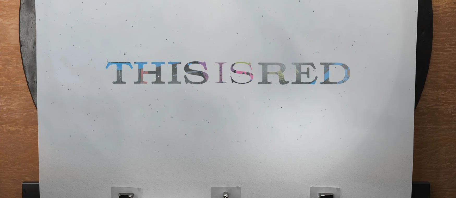 A white piece of paper on a gray surface with colorful, rainbow-like text that reads 'THIS IS RED' with some visible black ink smudges.