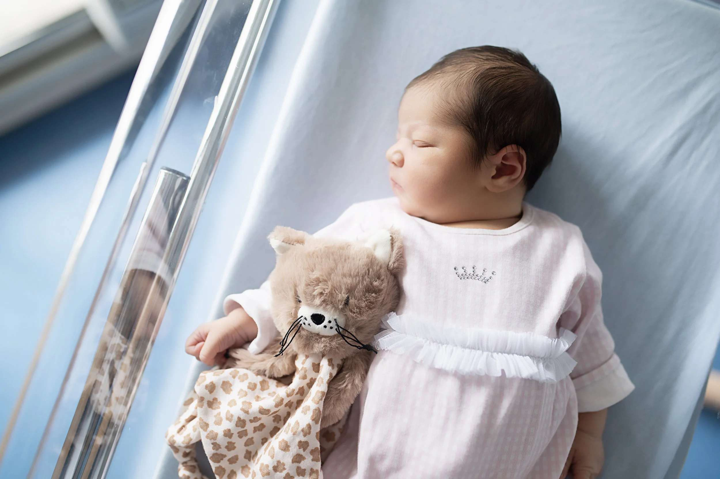 Un bébé endormi dans une bassinette, tenant un doudou en forme de lion avec une robe à motif léopard.