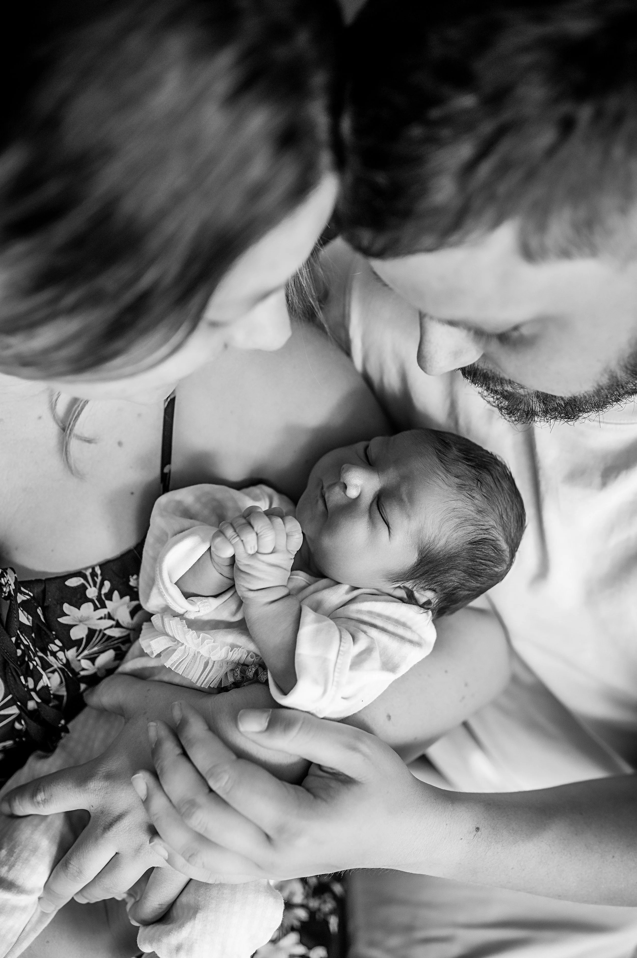 Une famille regarde tendrement un bébé petit, qui dort, dans leurs bras, dans une ambiance douce.