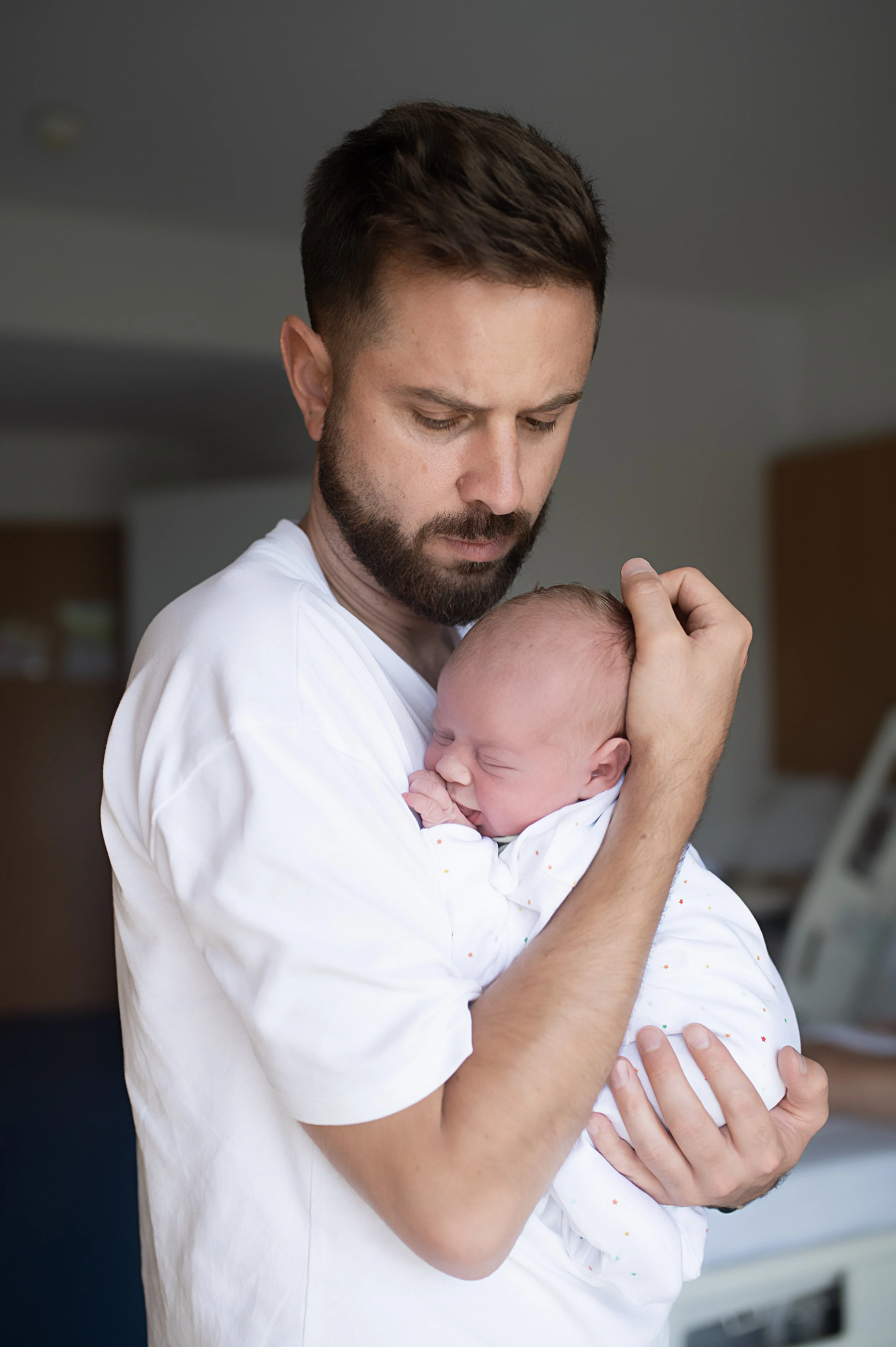 Un homme tient un bébé endormi dans ses bras, dans une pièce intérieure.