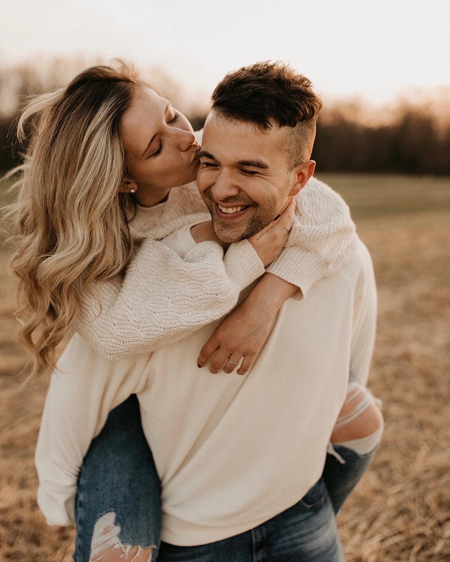 A couple enjoying a moment outdoors during sunset, with the woman giving a kiss on the man's cheek as he smiles.