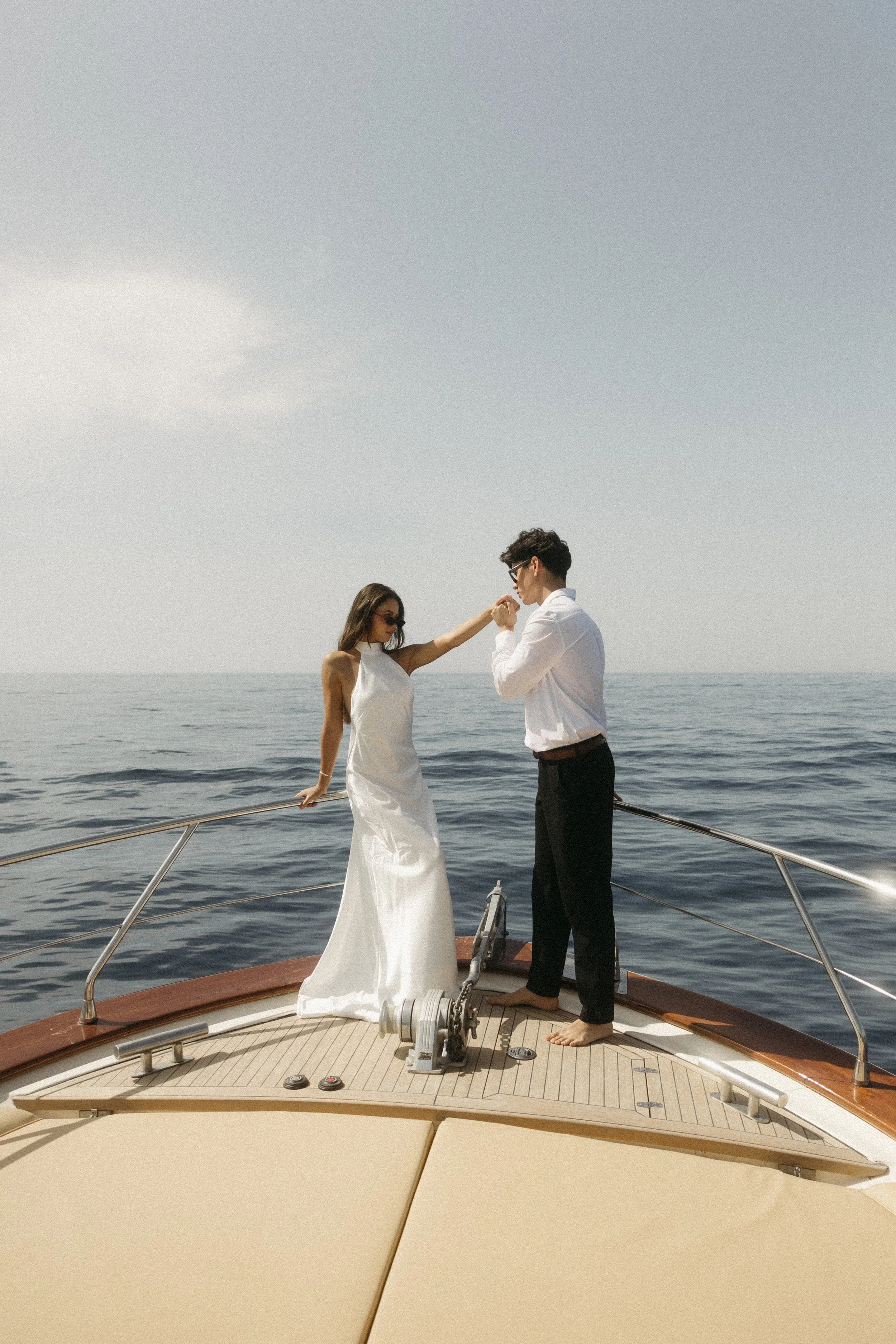 A couple dancing on the deck of a yacht at sea, with both wearing formal attire and sunglasses.