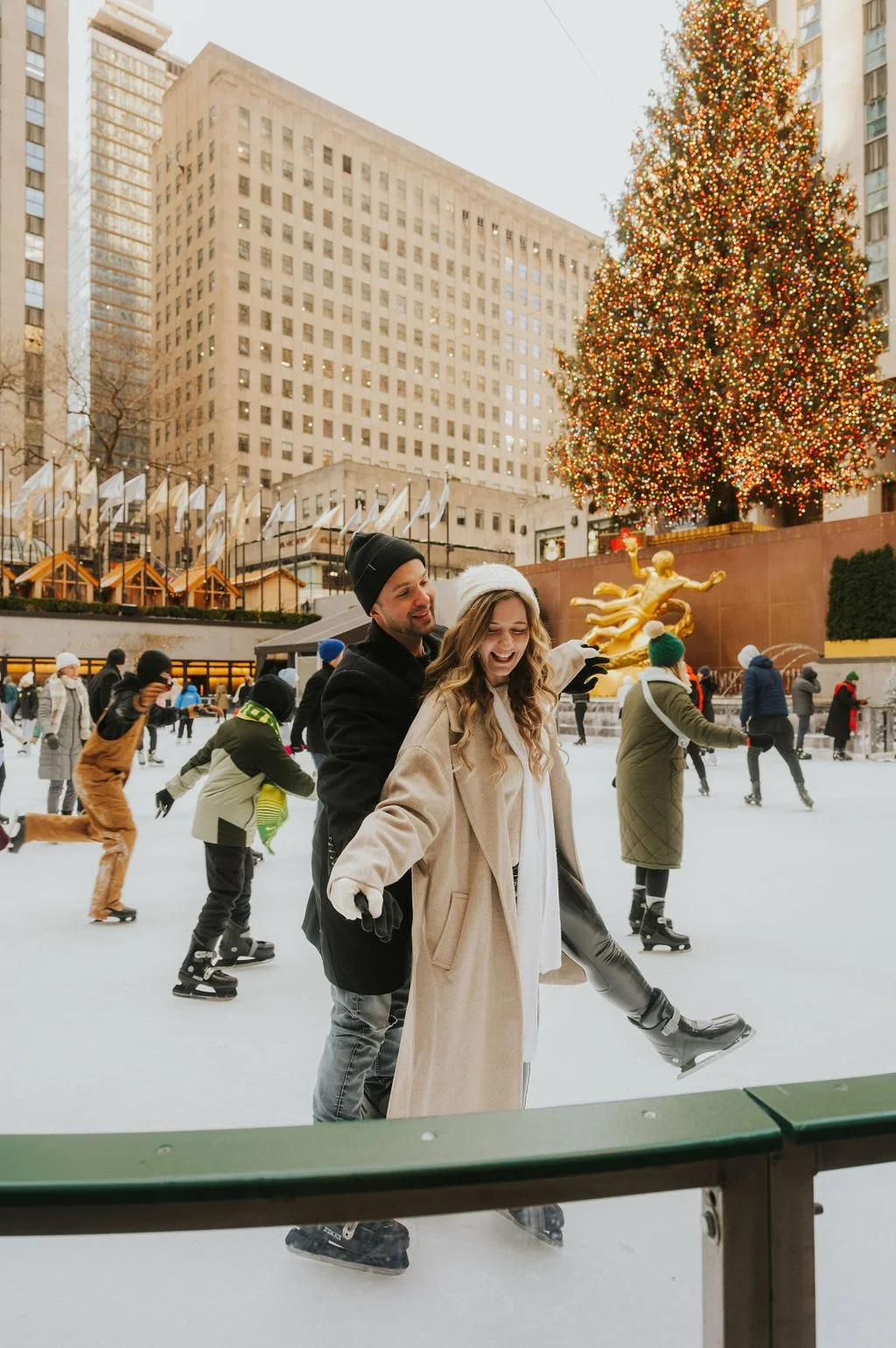 People ice skating outdoors in front of a large, decorated Christmas tree in a city plaza.