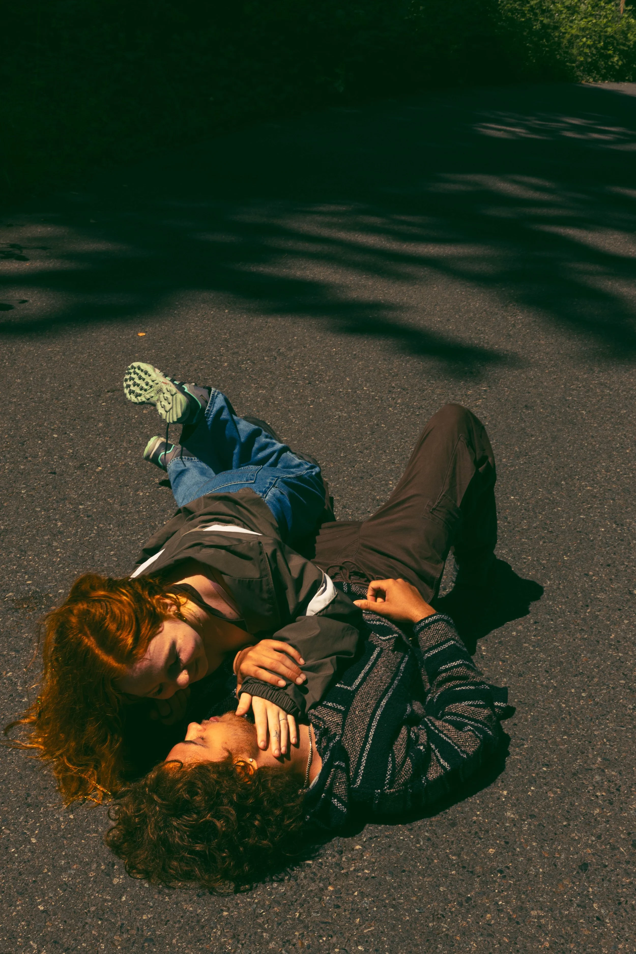 A woman and a man lying on the ground, with the woman kissing the man's neck, on a dark street at night.