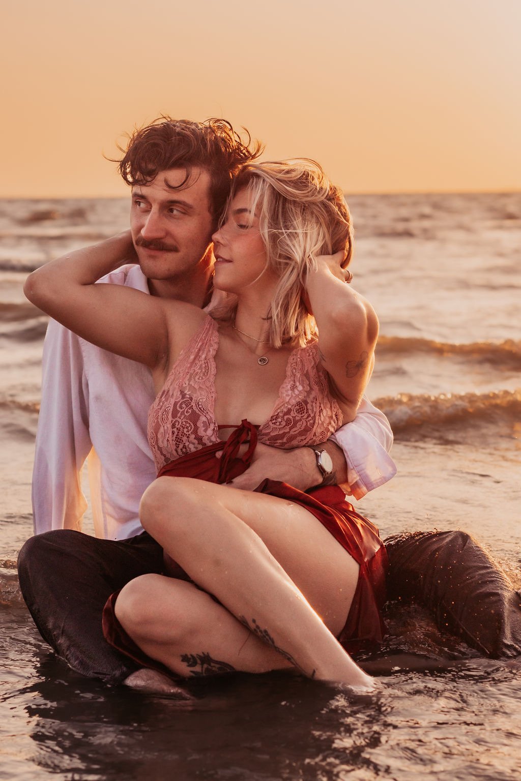 A couple sitting in the ocean at sunset, embracing each other lovingly.