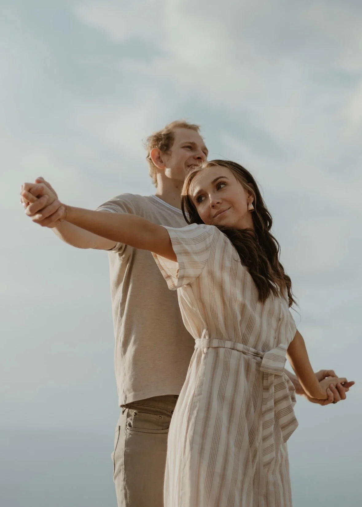 A woman and a man dancing together outdoors under a cloudy sky, holding hands and smiling.